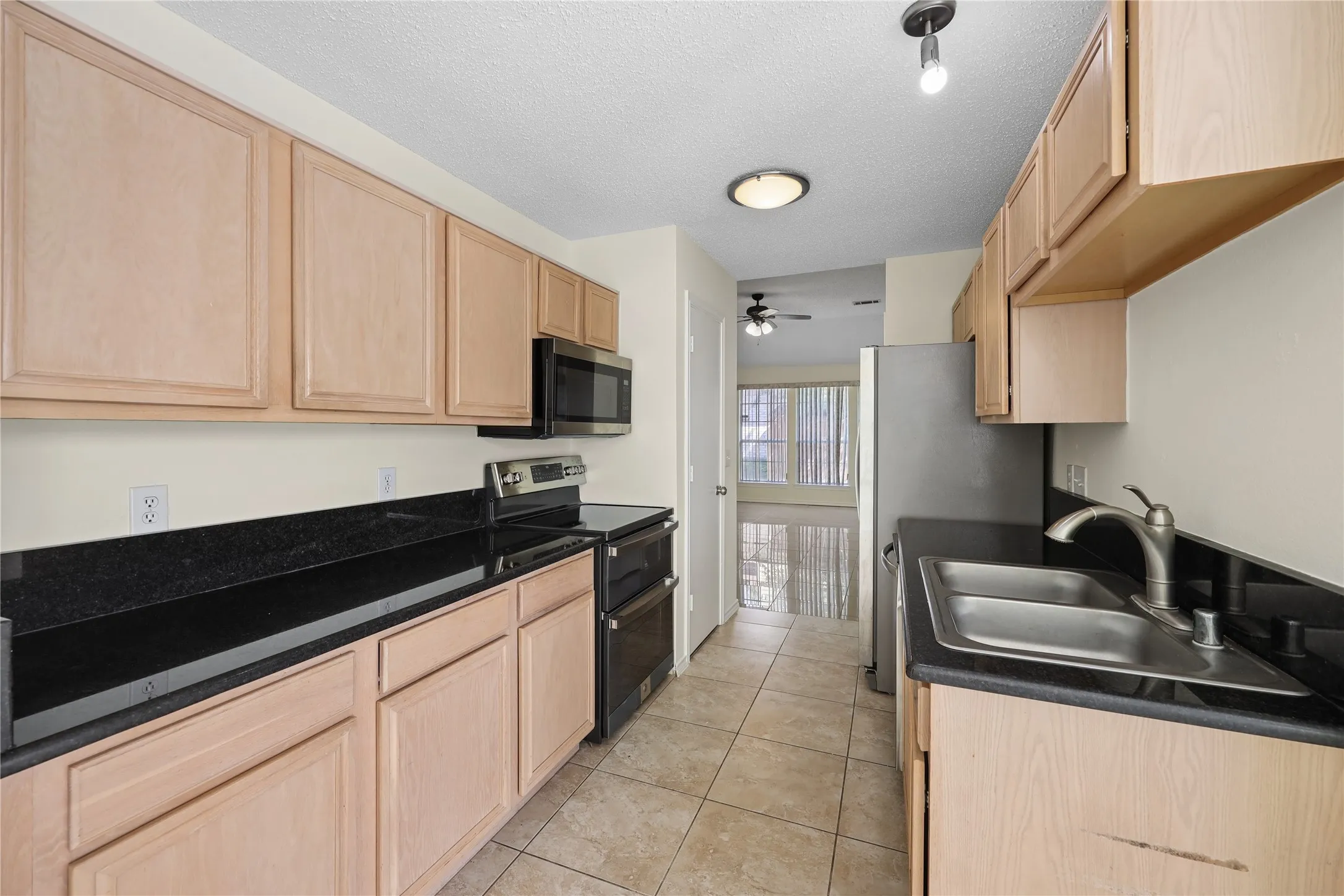 Kitchen featuring light-finish cabinetry, dark stone countertops, stainless steel appliances, dual-basin sink with high-arch faucet, and tile flooring