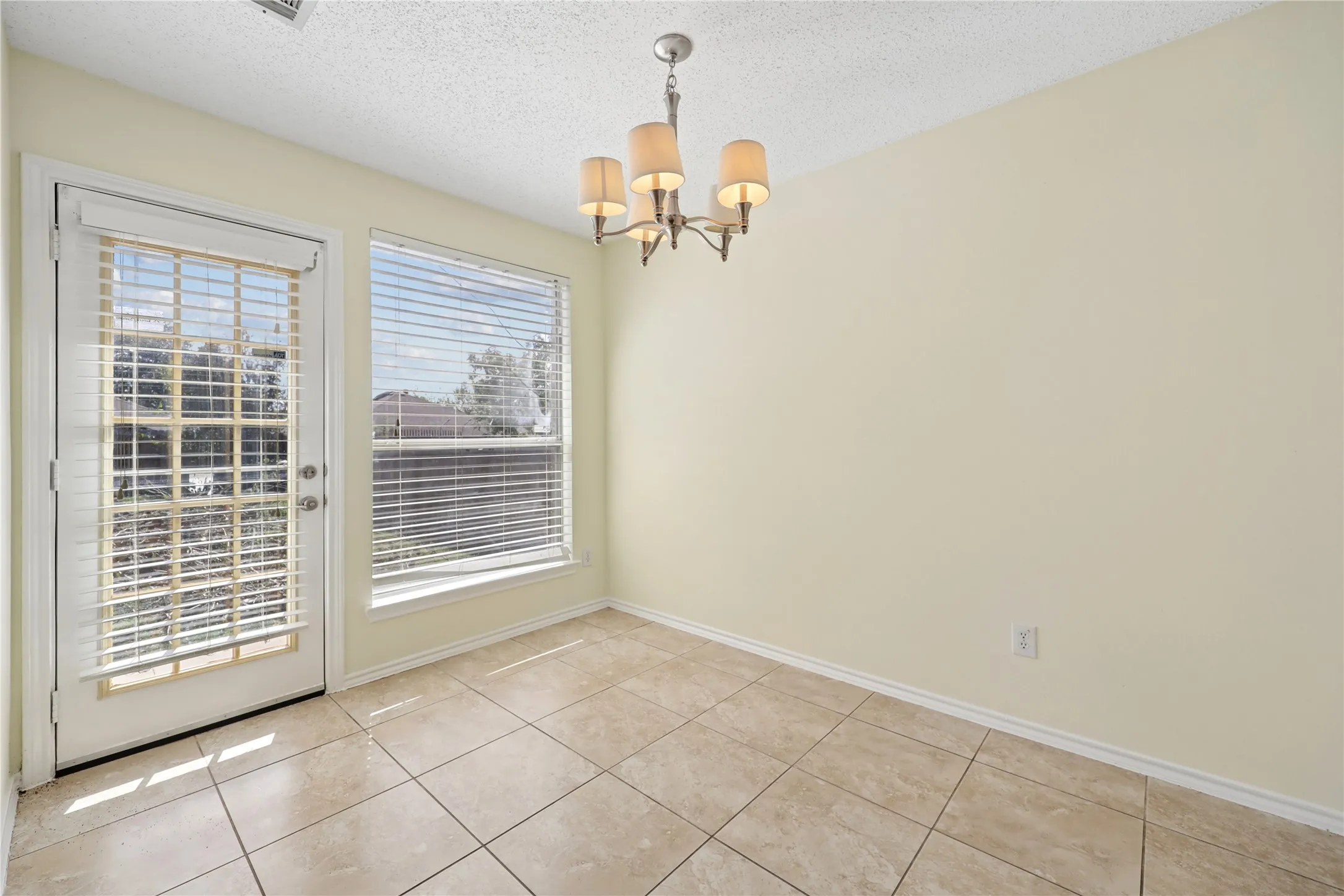 Neutral-toned ceramic tile flooring, five-light traditional chandelier, multi-pane glass door, and large rectangular window with horizontal blinds