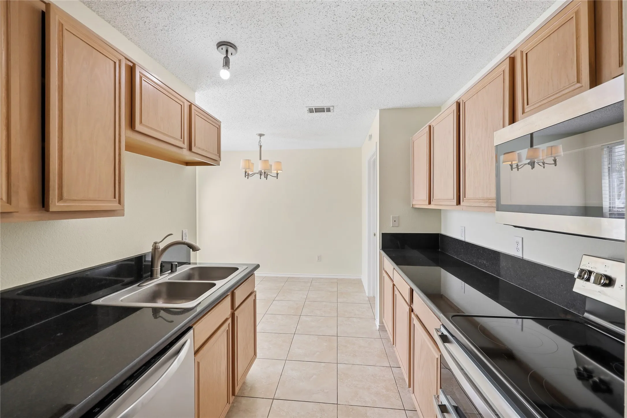 Kitchen featuring flat-panel wood cabinetry, black solid-surface countertops, dual-basin stainless steel sink, ceramic tile flooring, and built-in microwave