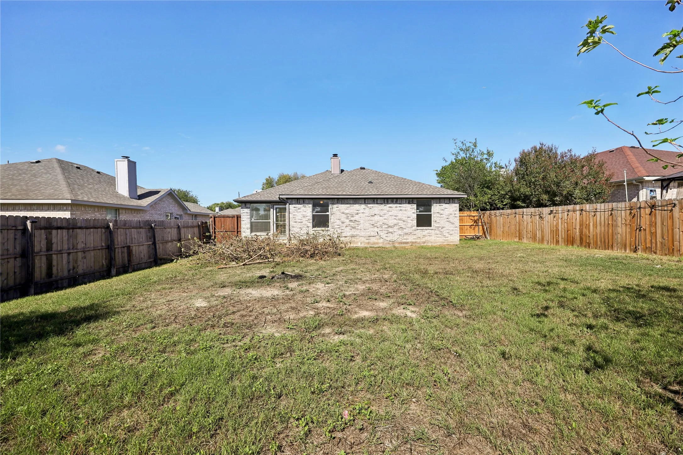 Rear exterior featuring a brick facade, roof chimney, and enclosed wooden perimeter fencing