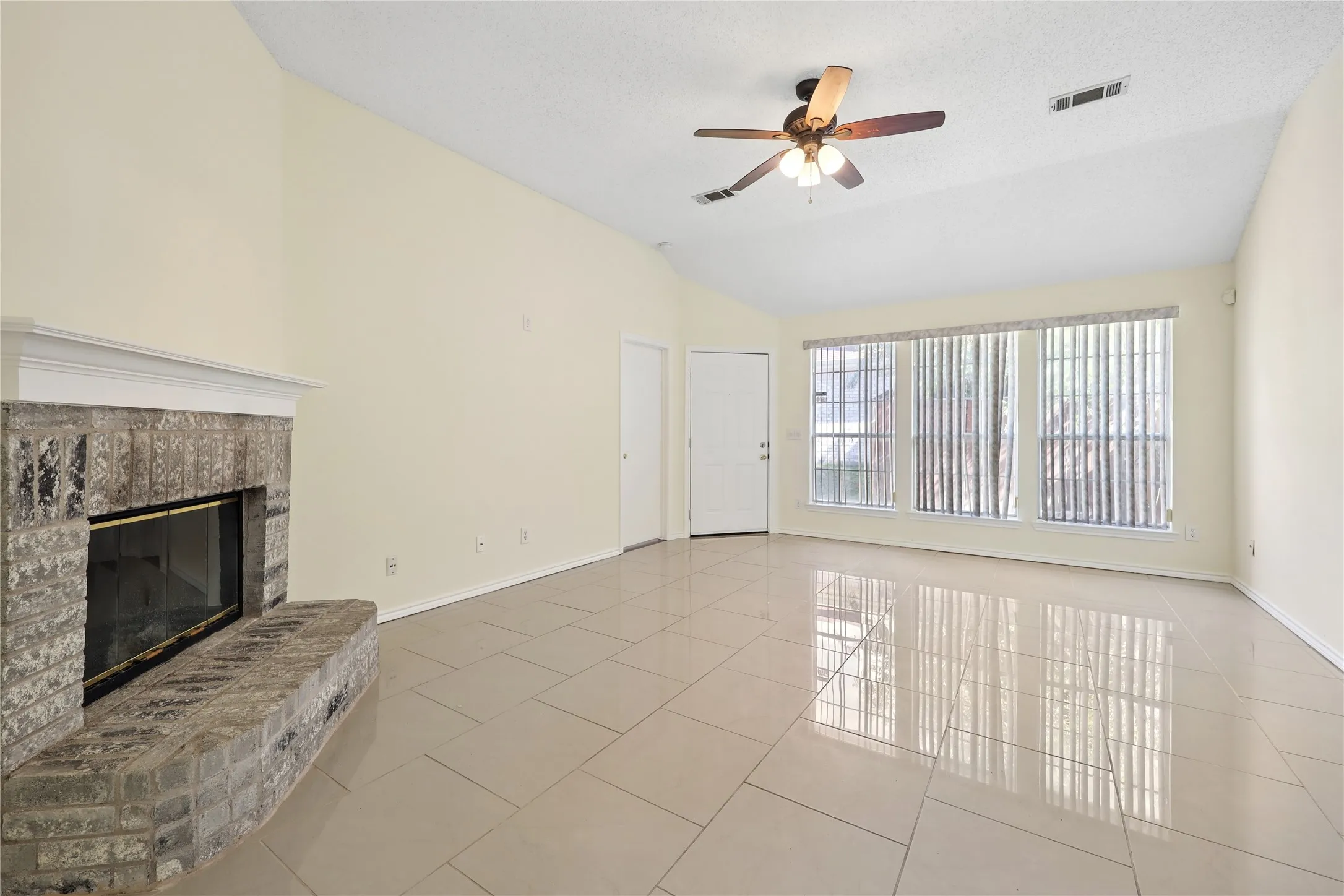 Vaulted ceilings with a ceiling fan, stone-surround fireplace, large-format tile flooring, and oversized windows with vertical blinds