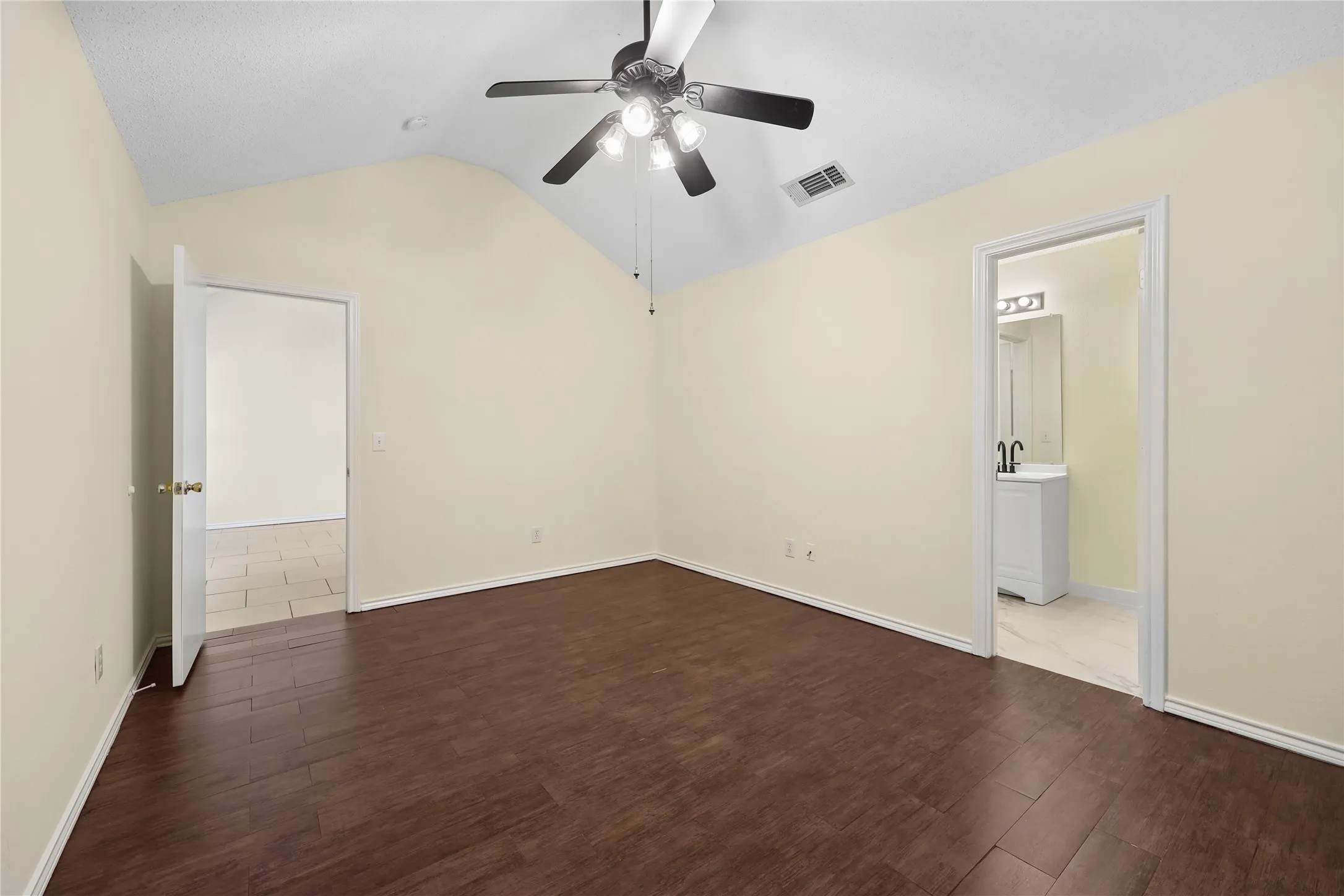 Vaulted ceiling featuring a central multi-light fan, dark wood-finish flooring, and neutral wall tones