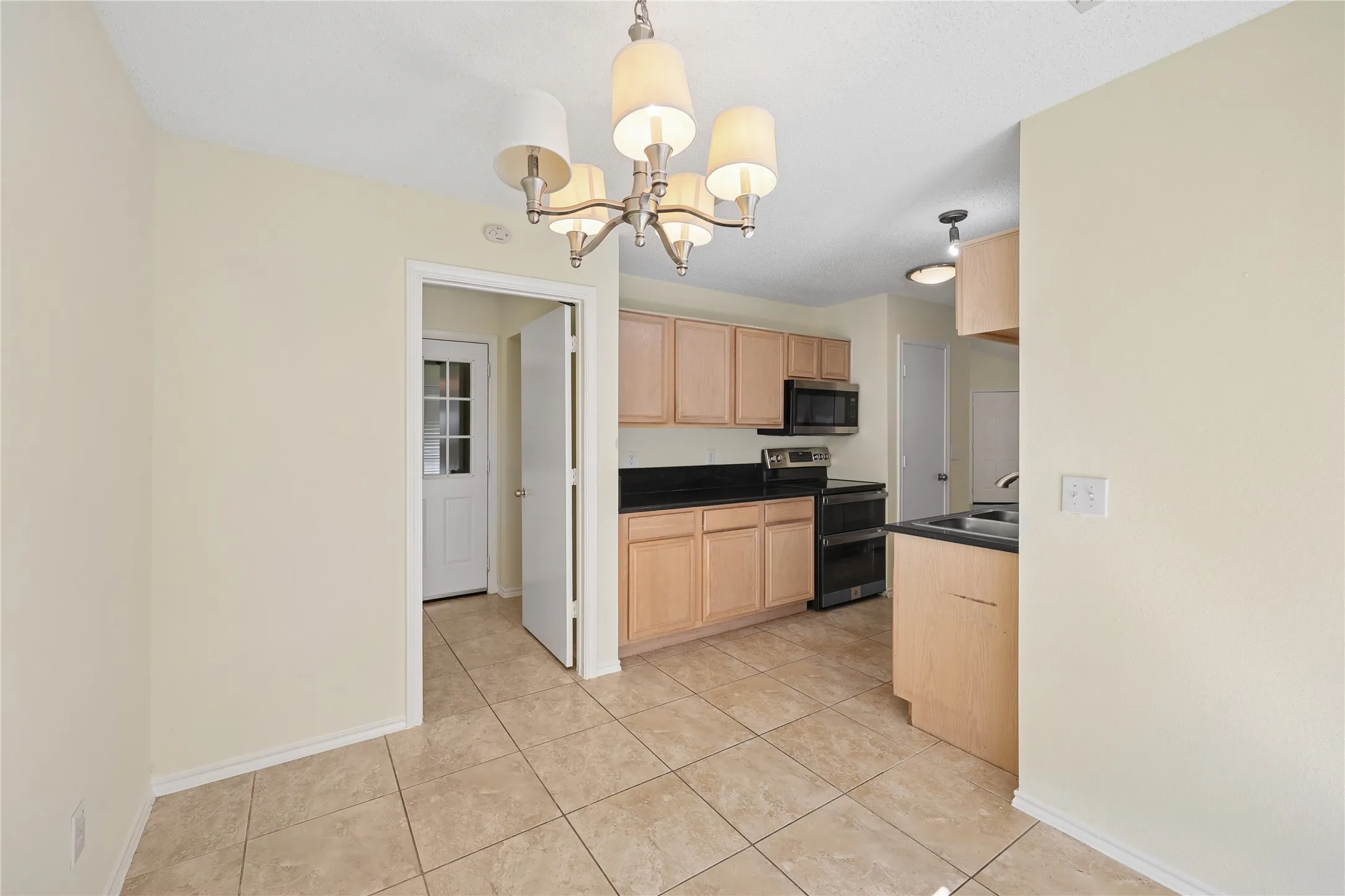 Kitchen featuring light-finish cabinetry, dark solid-surface countertops, built-in black appliances, tile flooring, and a multi-arm chandelier
