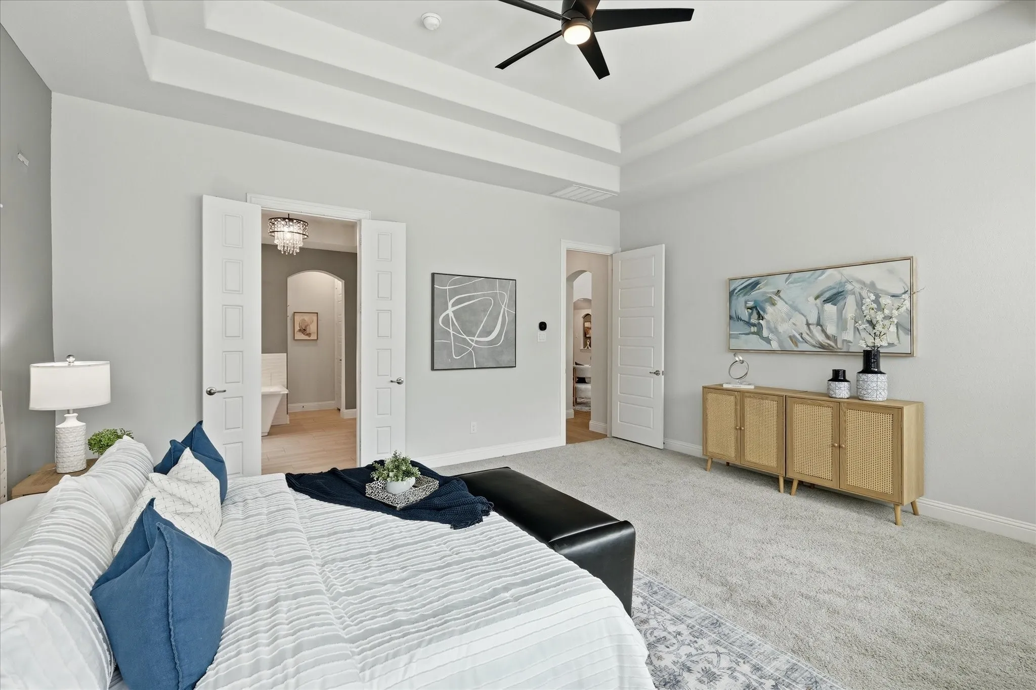 Spacious primary bedroom featuring a tray ceiling, expansive bay windows with plantation shutters, and reading area.