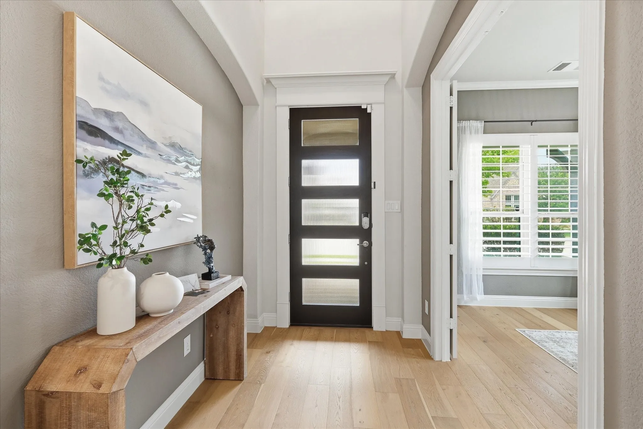 A glass-paneled front door welcomes abundant natural light into the foyer, showcasing the stunning blonde flooring that runs throughout the main living areas.