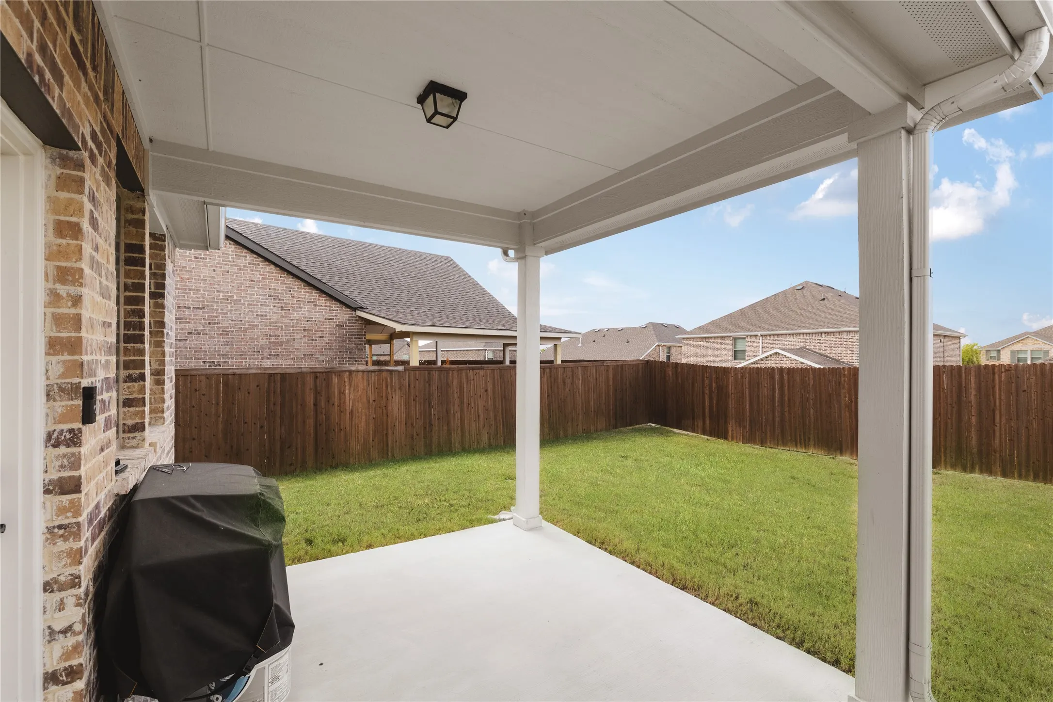 Covered concrete patio featuring a brick exterior wall, solid wood fencing, and a built-in ceiling light fixture