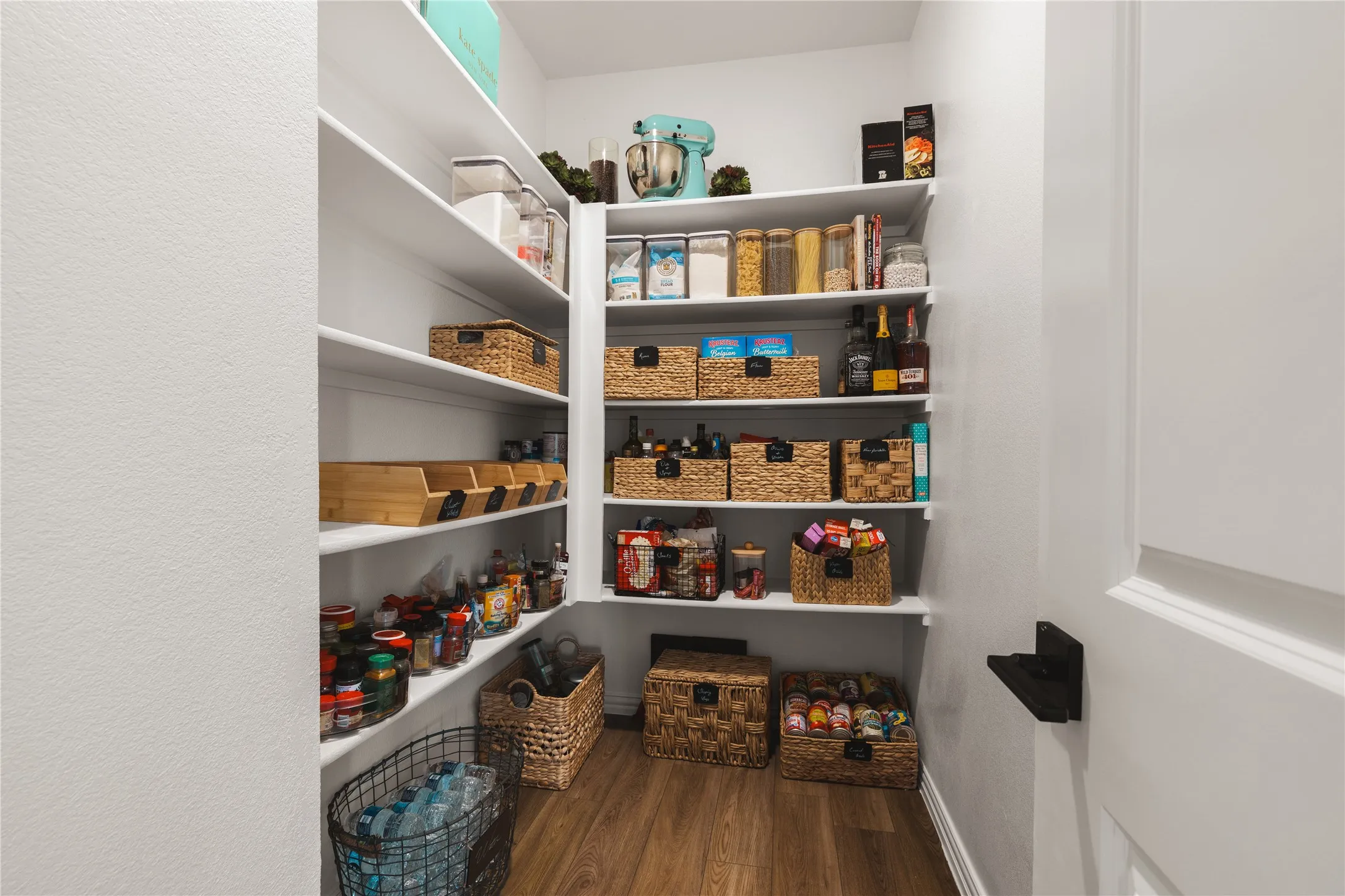 Walk-in pantry featuring white wrap-around shelving and wood-finish flooring
