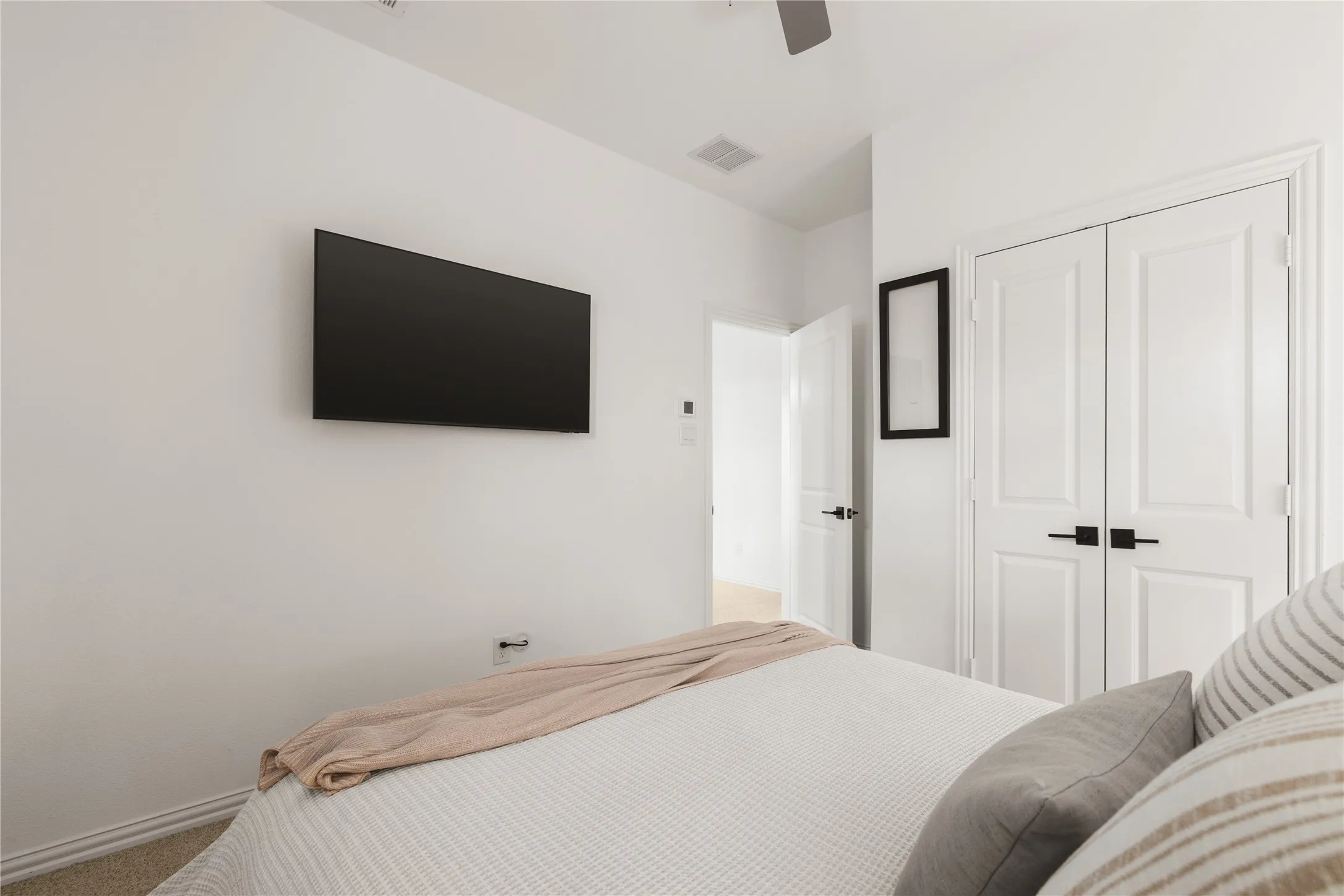 Interior room featuring neutral wall paint, carpet flooring, a ceiling fan, and double-panel closet doors with matte black hardware