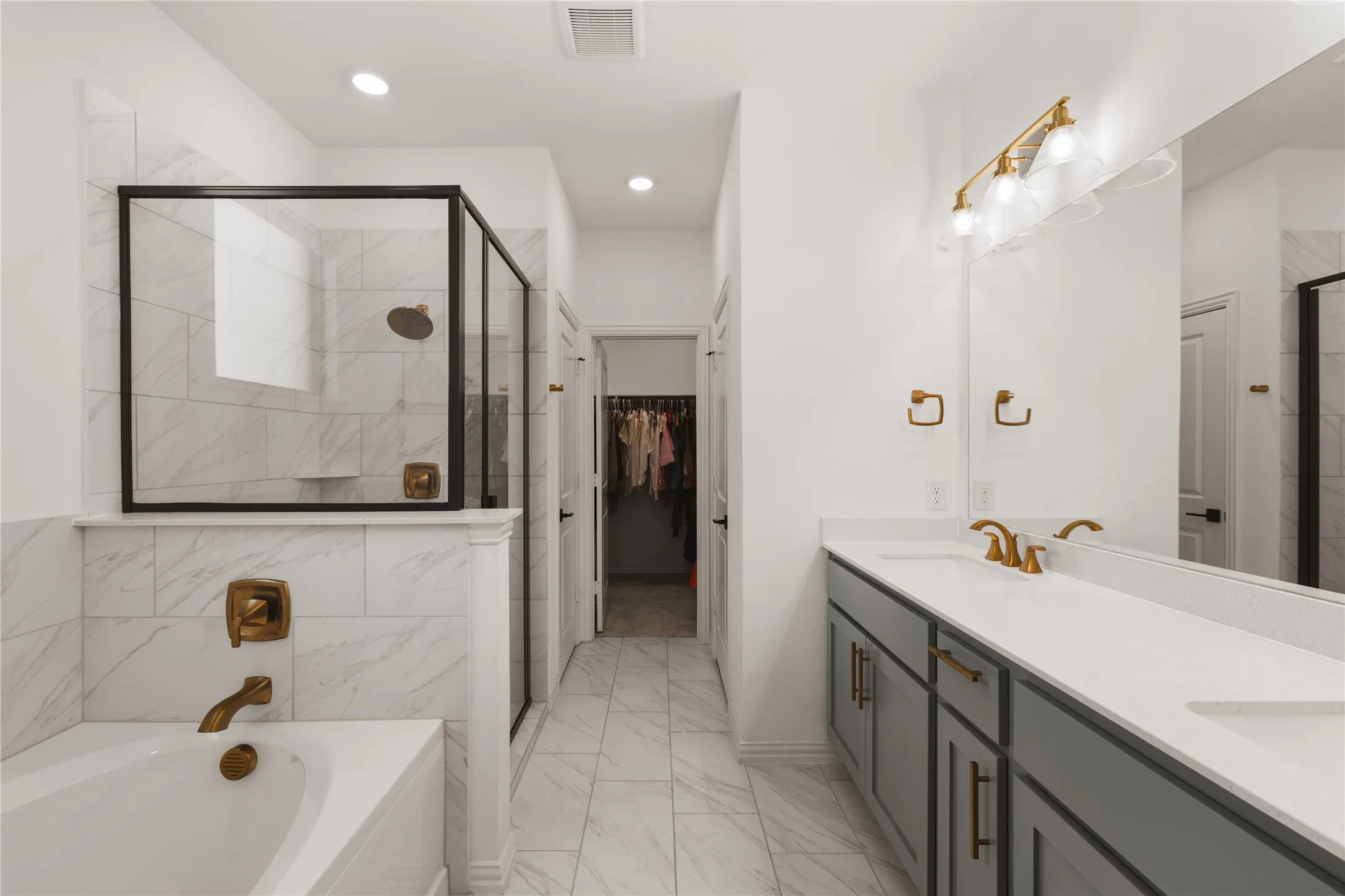 Bathroom featuring a dual-sink vanity with solid-surface countertops, walk-in shower with matte black framing, soaking tub, and stone-finish tile flooring