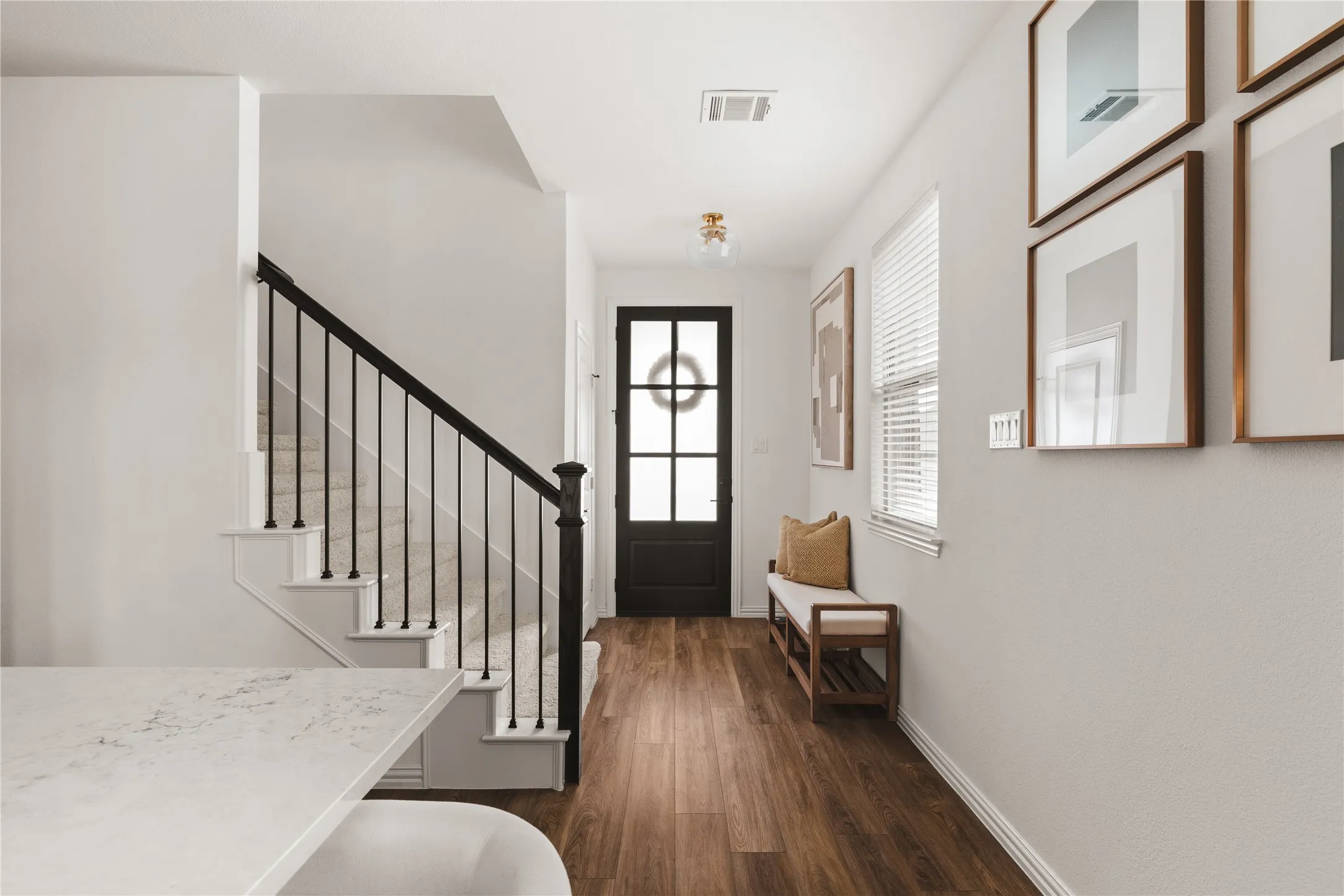 Entryway featuring wood-finish flooring, staircase with a matte black metal railing, glass-paneled entry door, and flush-mount brass light fixture