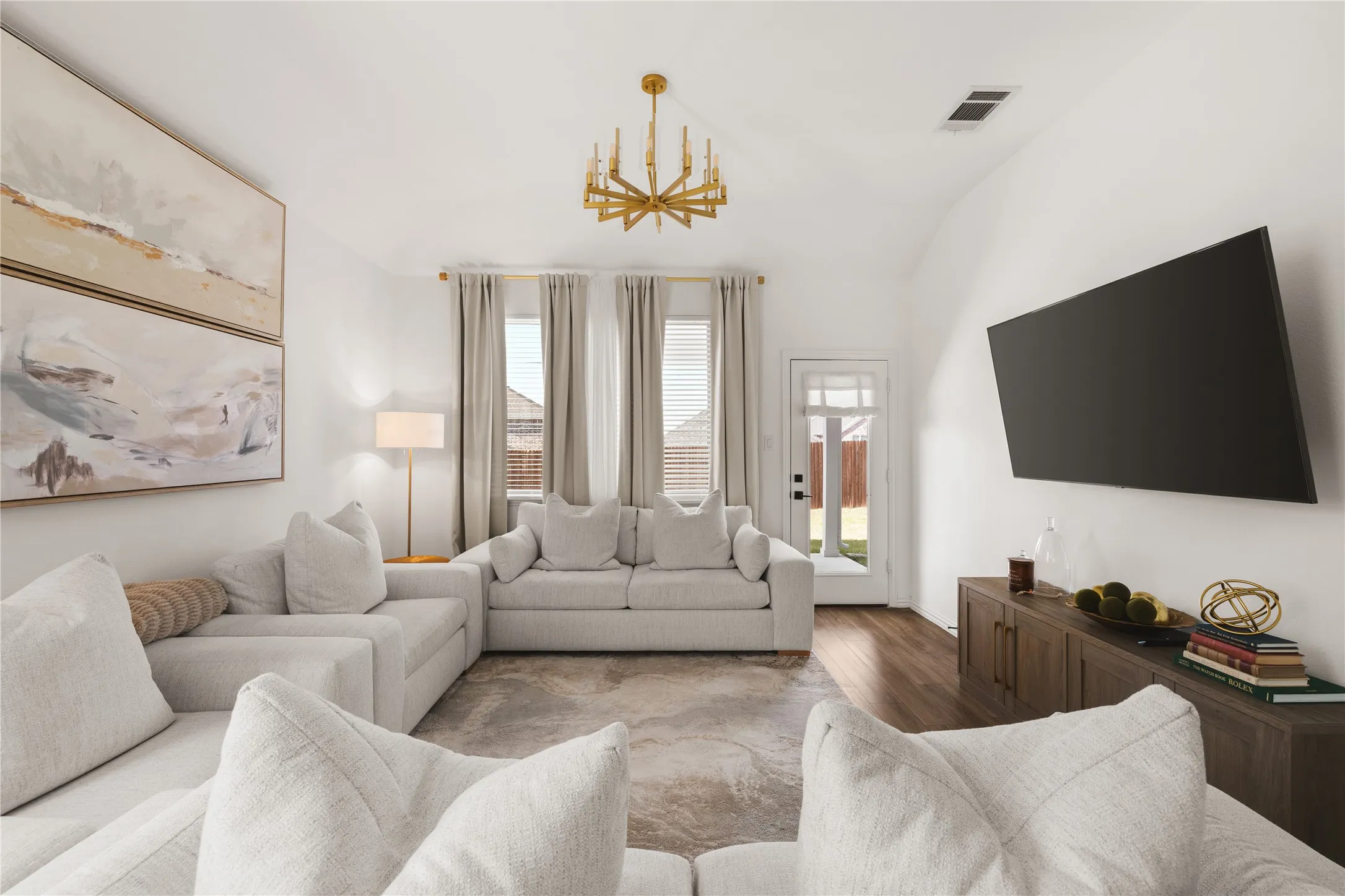 Vaulted ceilings, wood-finish flooring, gold-tone multi-arm chandelier, and glass-paneled exterior door