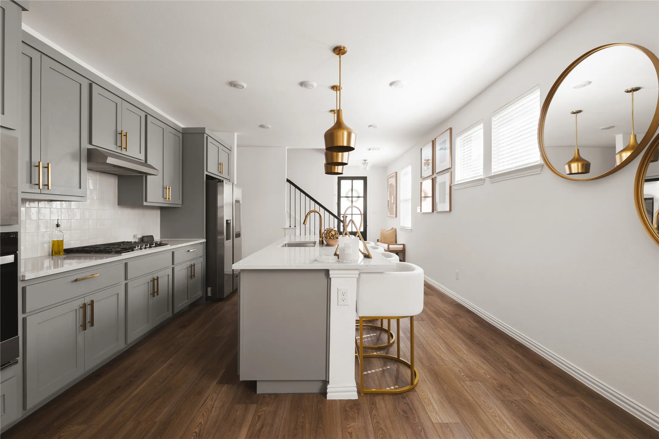 Kitchen featuring grey Shaker-style cabinetry, a central island with a quartz countertop, wood-finish flooring, brass-tone pendant lighting, and a white subway tile backsplash