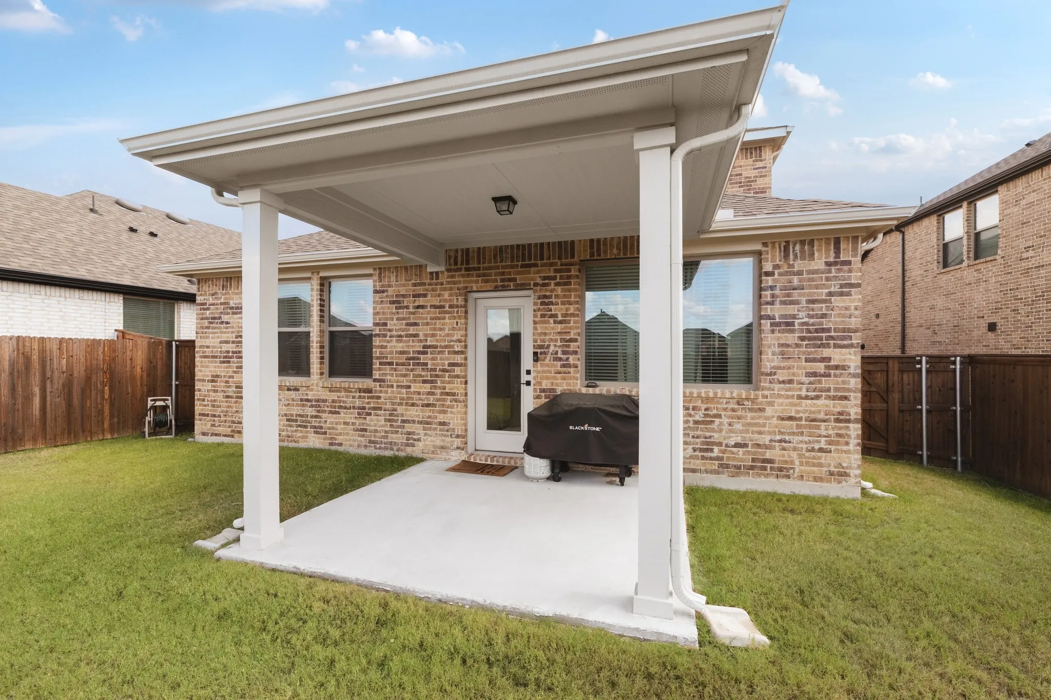 Covered patio featuring a concrete slab, brick exterior cladding, and wood-fence perimeter