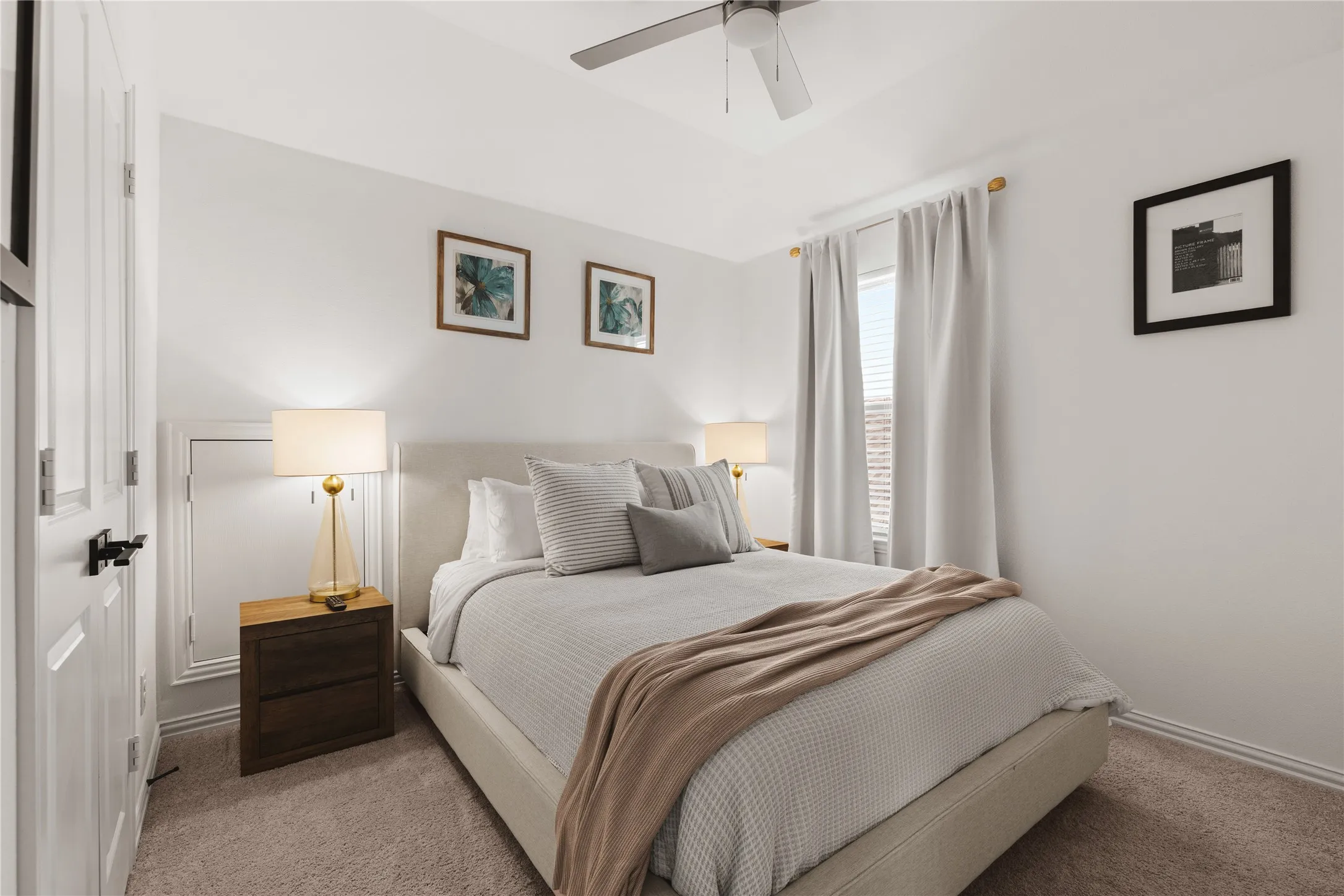 Neutral-toned carpeted flooring, multi-panel interior door with matte black hardware, and ceiling-mounted fan with light fixture
