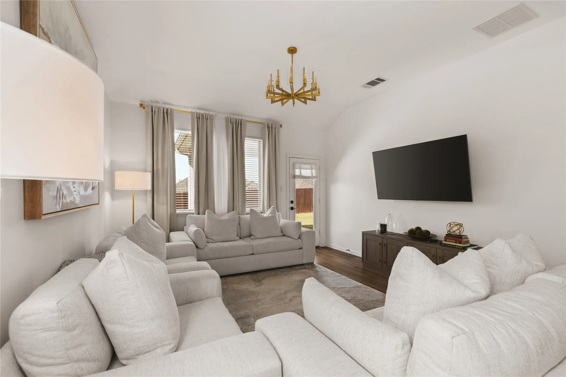 Vaulted ceilings, wood-finish flooring, gold-tone chandelier, and natural light from tall windows