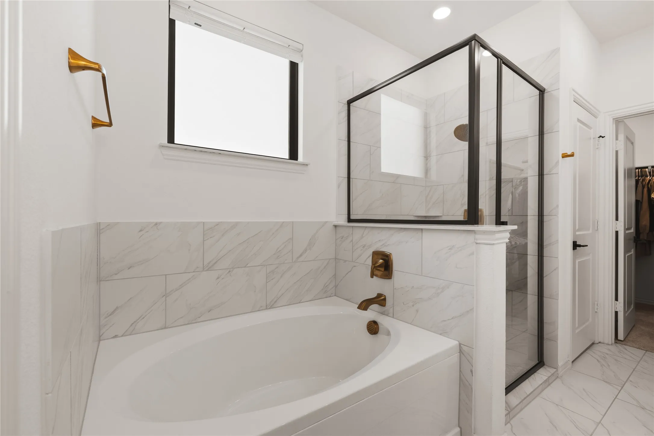 Soaking tub with bronze-tone fixtures, glass-enclosed shower with a matte black frame, and large-format stone-patterned tile wall surrounds