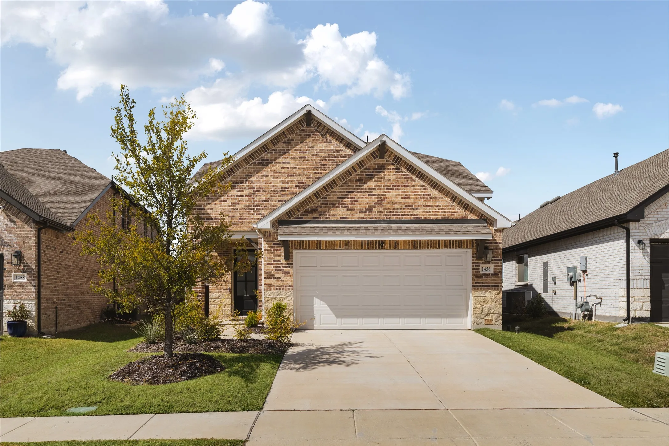 Brick and stone exterior featuring a double-gabled roofline, front-facing two-car garage, and concrete driveway