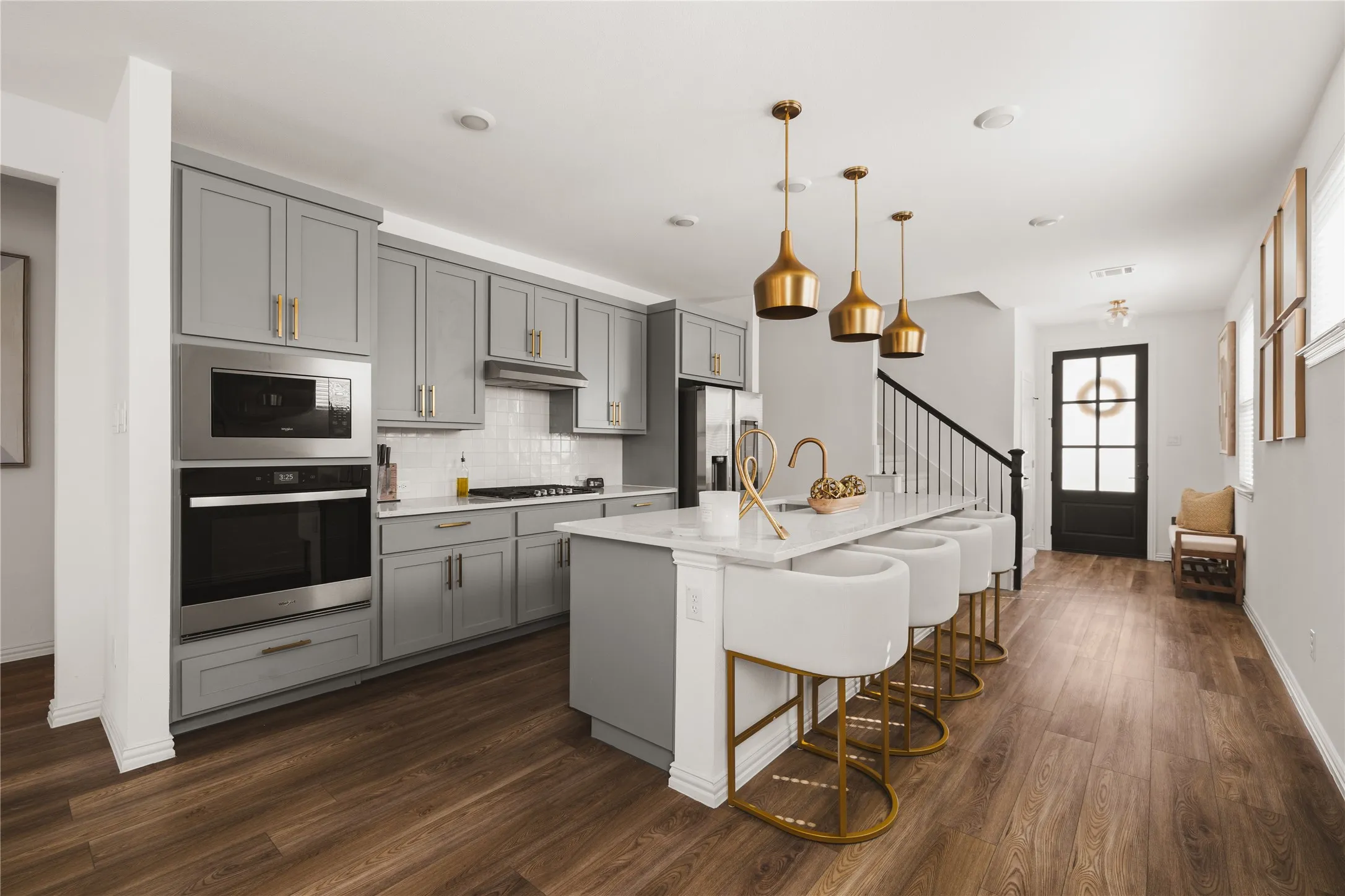 Kitchen featuring grey Shaker-style cabinetry, a central island with a quartz countertop, stainless steel double wall ovens, wood-finish flooring, and metallic pendant lighting