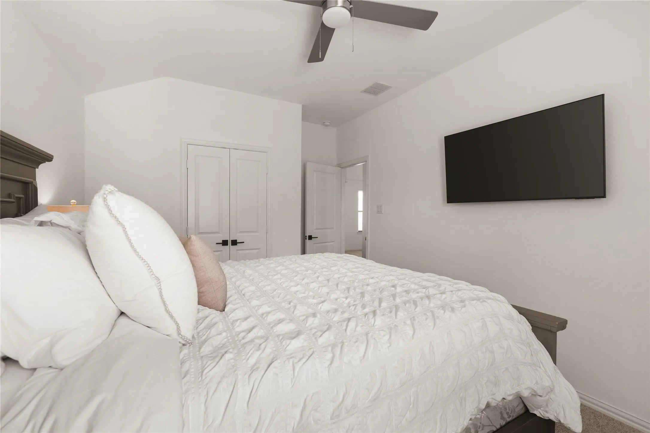 Vaulted ceilings, neutral walls, flush-mount ceiling fan with integrated lighting, and white interior doors with matte black hardware