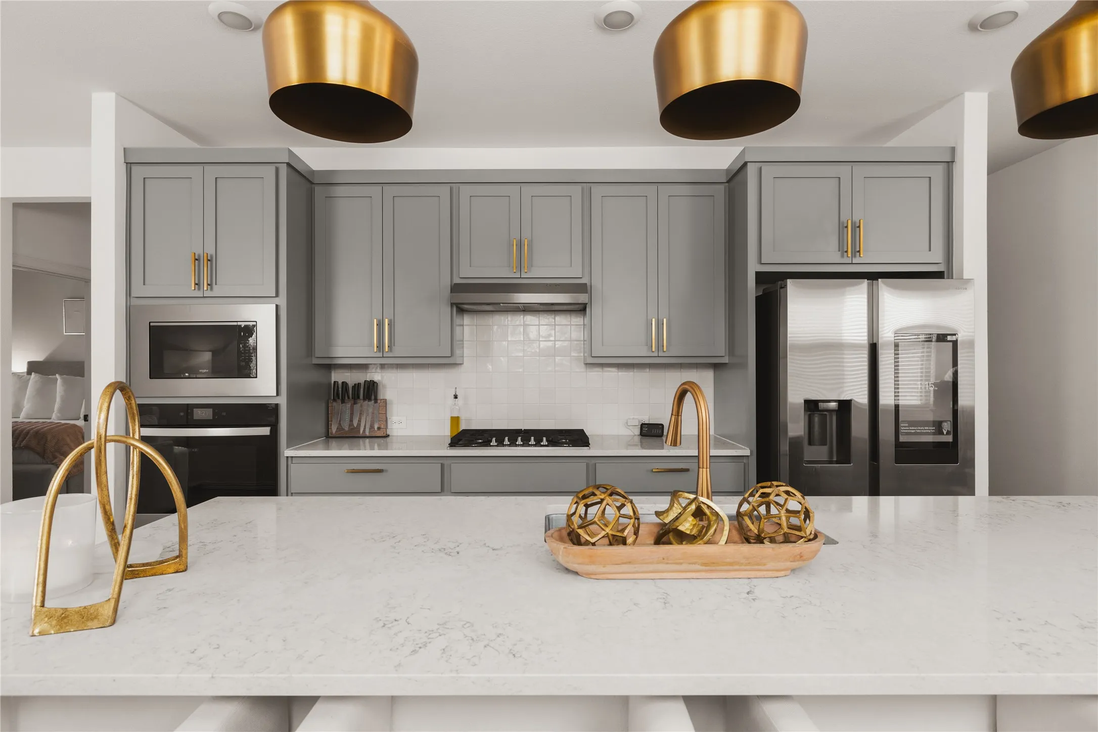 Kitchen featuring gray shaker-style cabinetry, a stone-finish island countertop, brass-tone hardware, pendant lighting, and stainless steel appliances