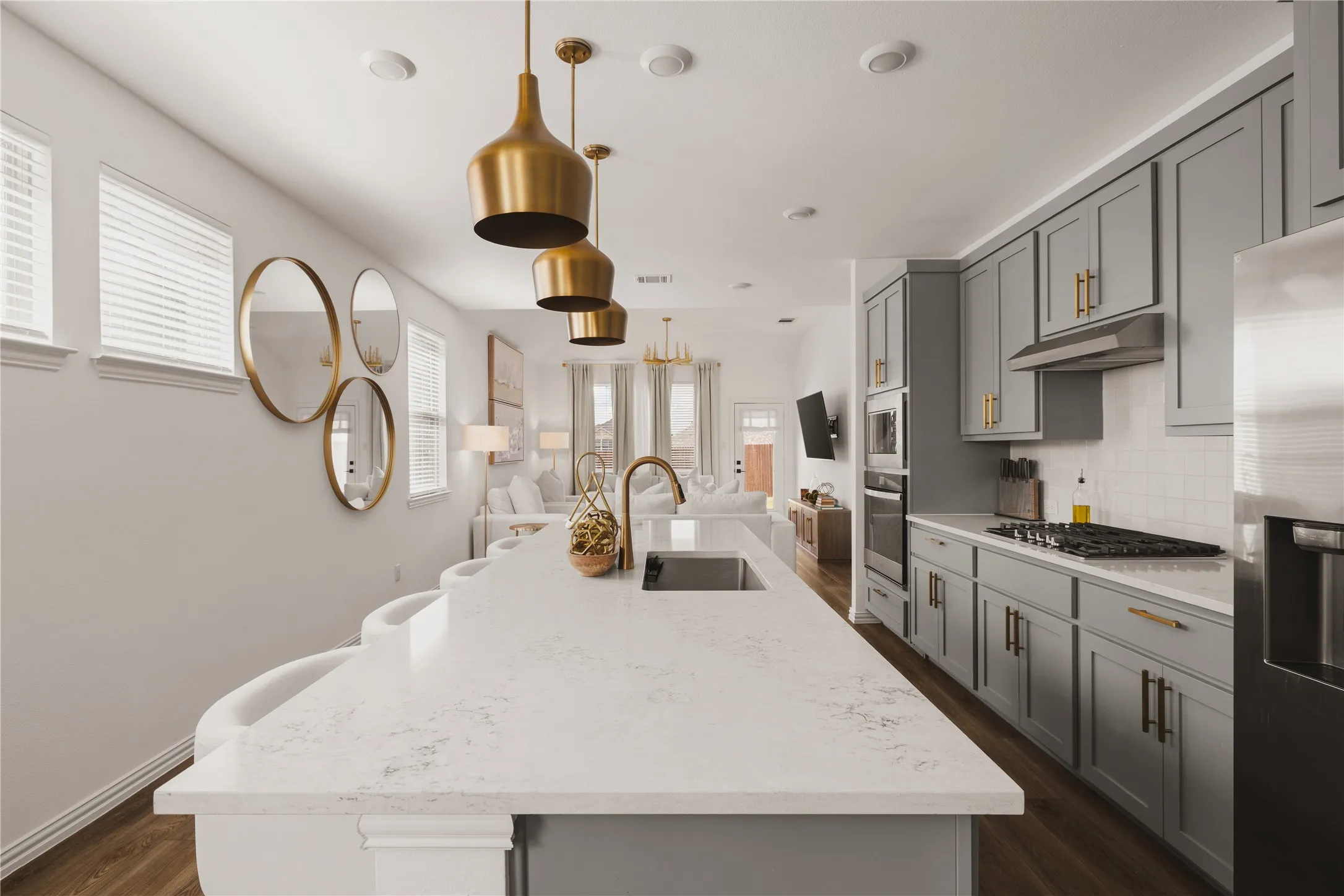 Kitchen featuring a quartz-topped island with an undermount sink, grey cabinetry with brass-finish hardware, built-in stainless steel oven, gas cooktop, and brass pendant lighting