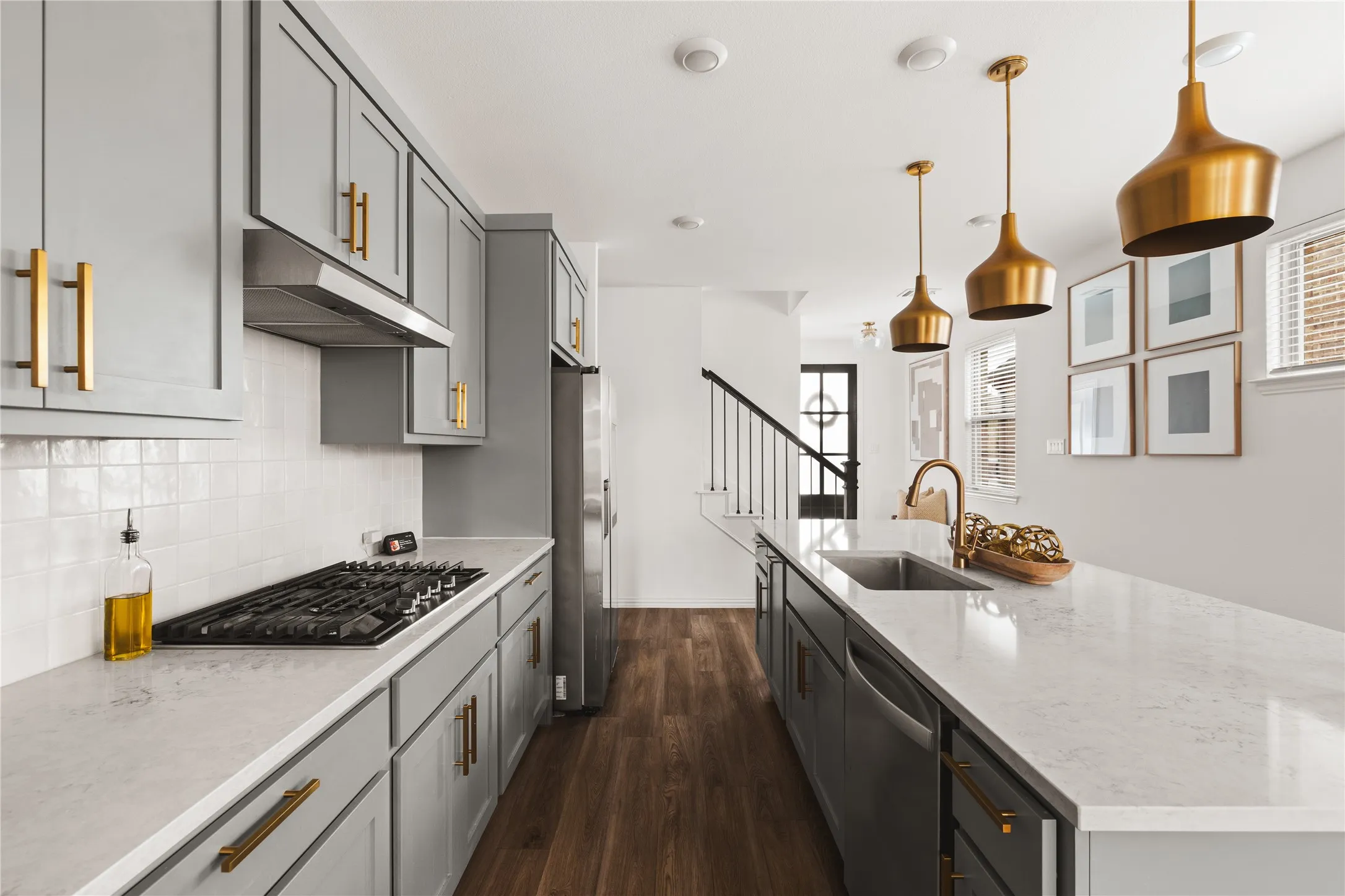 Kitchen featuring shaker-style cabinetry with brass-finish hardware, quartz countertops, a white tile backsplash, metal pendant lighting, and wood-finish flooring