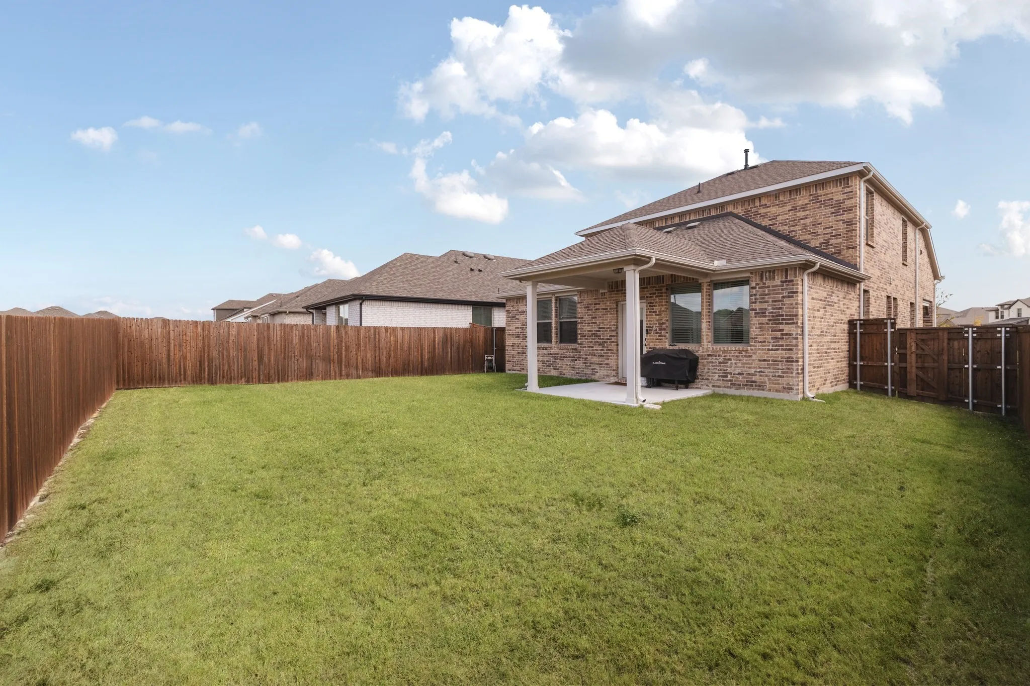 Brick exterior, covered rear patio, and enclosed backyard with wood fencing
