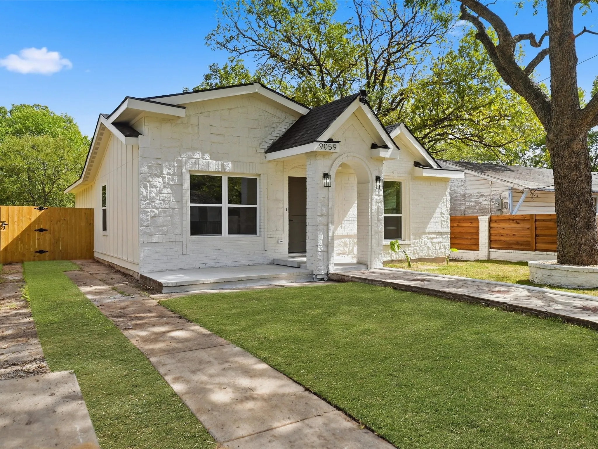 Exterior façade featuring white stone and vertical siding, covered entryway with arched portico, and wood-finish perimeter fencing