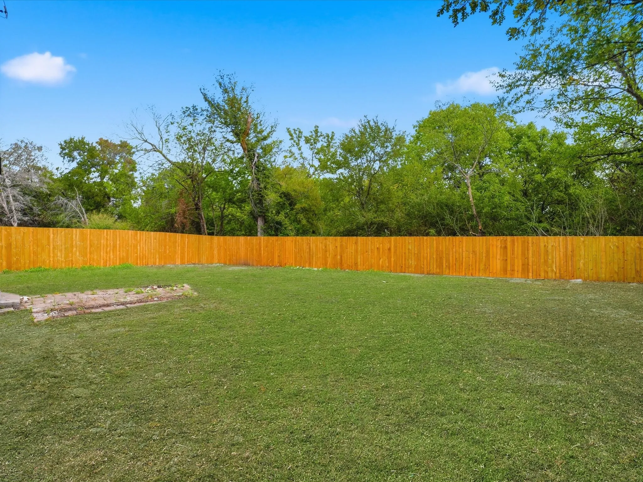 Expansive backyard featuring a large grass lawn, a wood-panel privacy fence, and mature trees