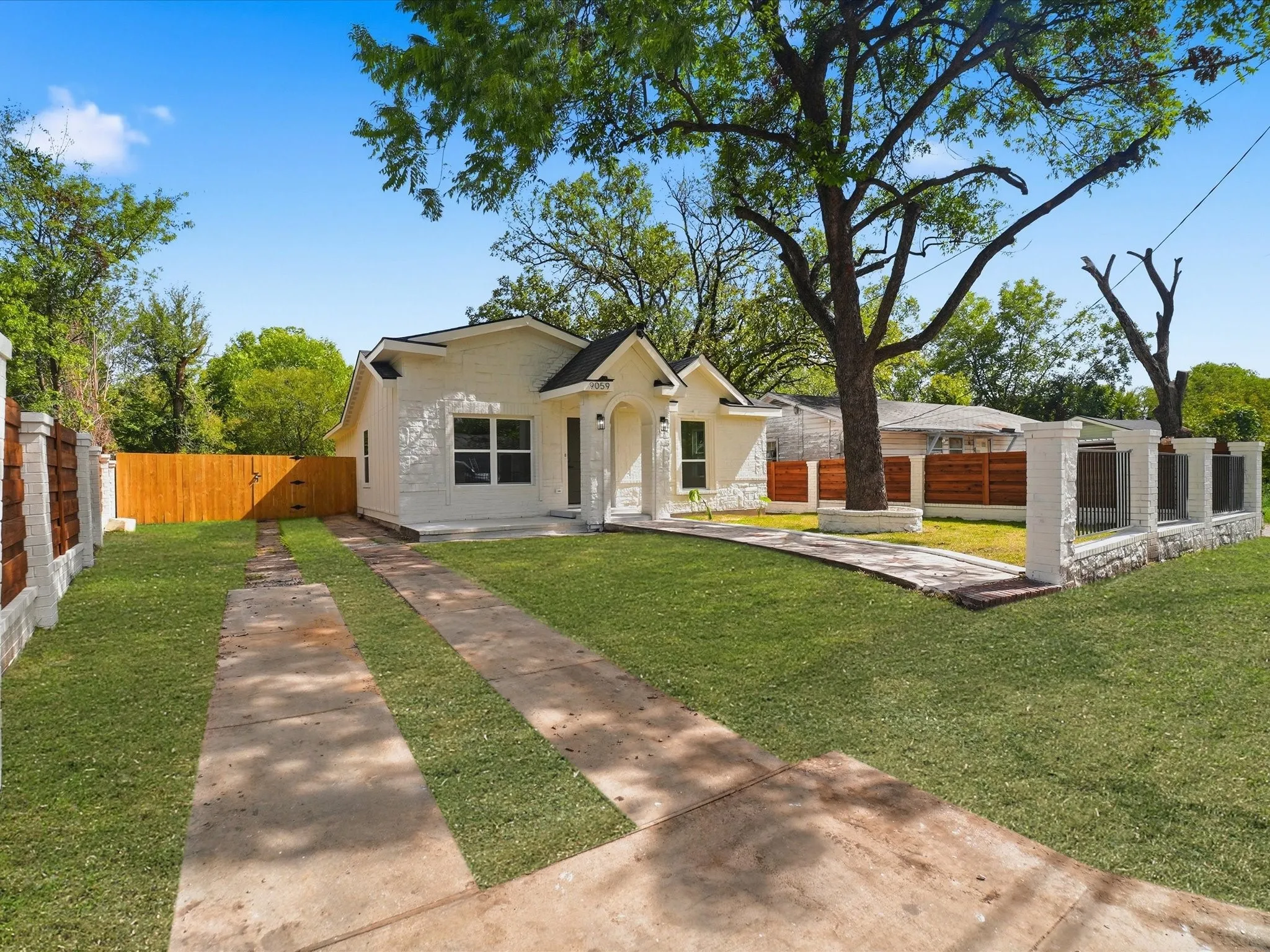 Single-story residence featuring a painted masonry exterior, covered front entryway, concrete ribbon driveway, and perimeter wood privacy fencing with masonry pillar accents