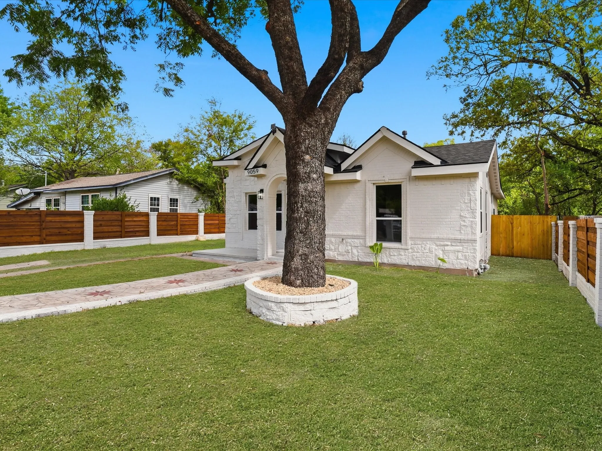 Painted brick exterior featuring a multi-gabled roofline, stone-finished masonry, wood-and-masonry perimeter fencing, and a stone-paver walkway