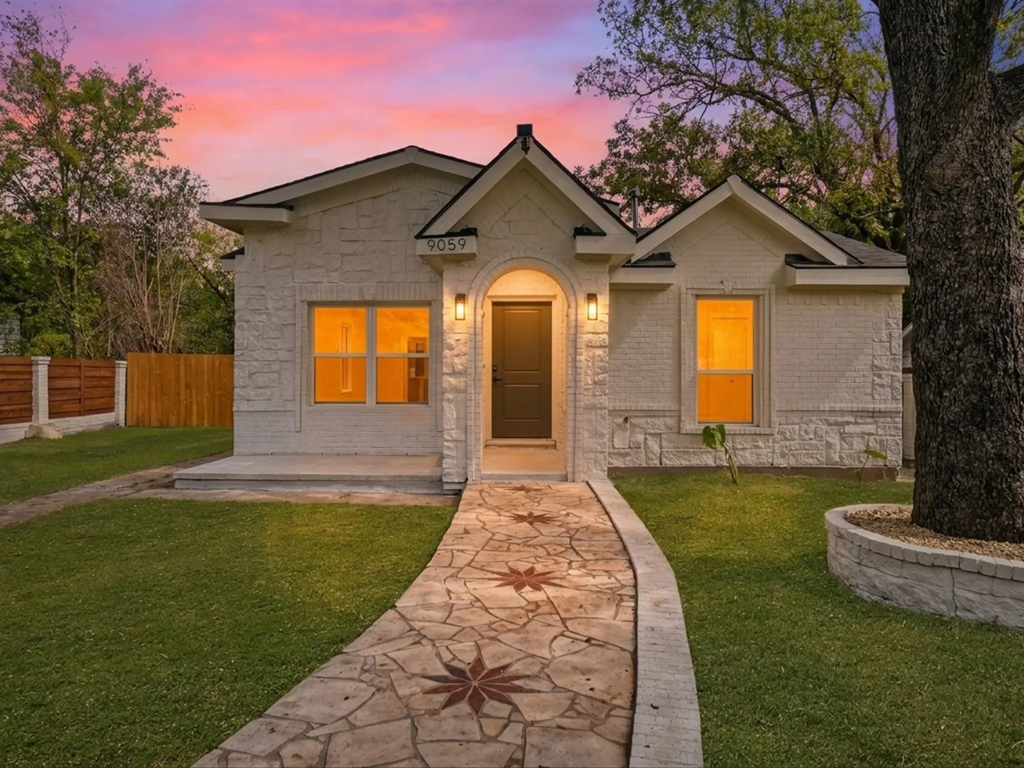Stone-veneer exterior with an arched entryway, decorative flagstone pathway, and a tiered stone tree planter