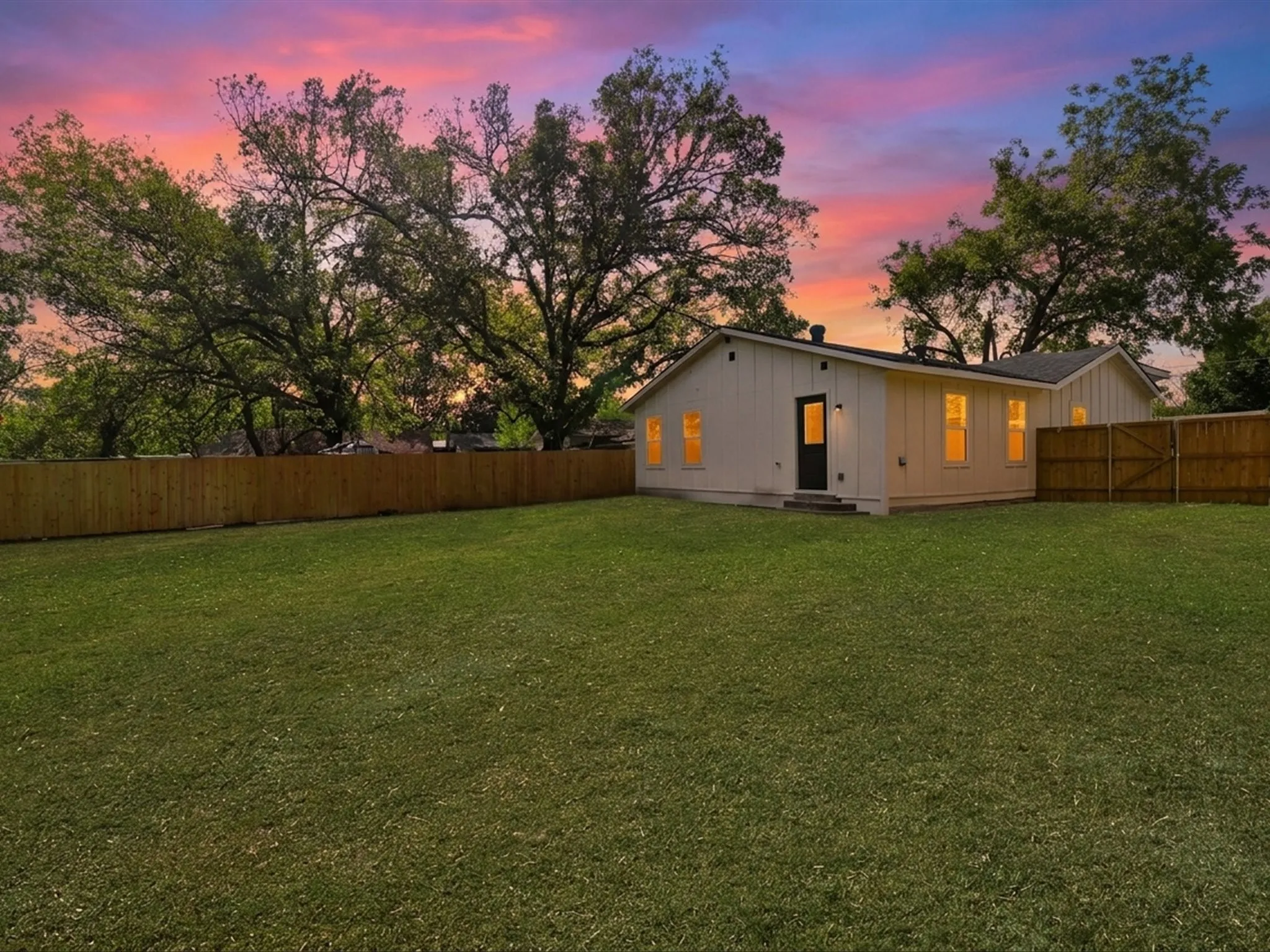 Expansive backyard featuring a level lawn, mature trees, and a full wood-fence perimeter
