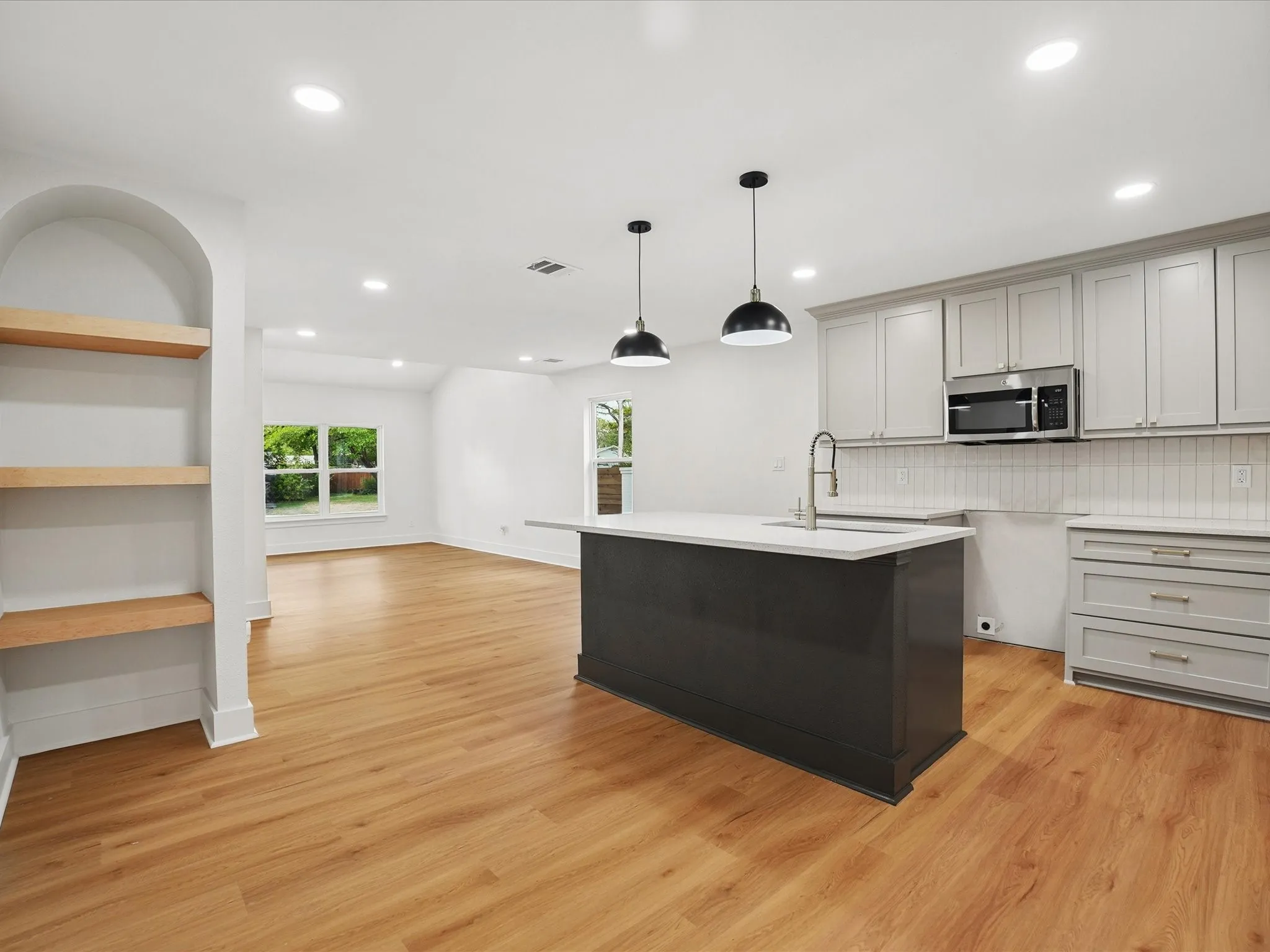 Kitchen featuring a dark-toned center island with light stone countertop, recessed lighting, wood-finish flooring, built-in recessed shelving, and a combination of grey cabinetry and stainless steel microwave