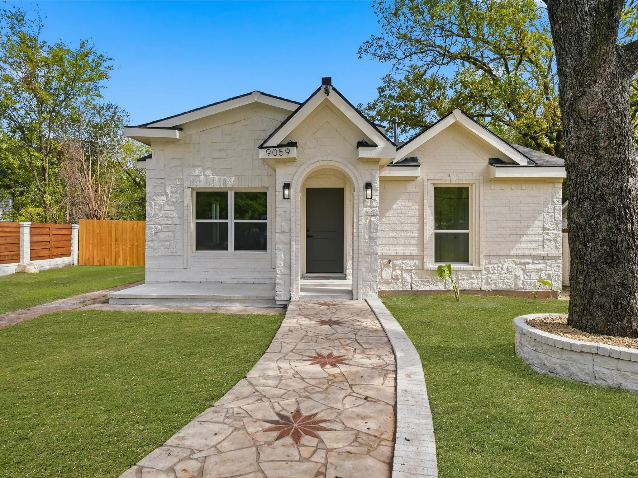 Exterior featuring painted brick and stone facade, arched entryway, custom stone-patterned walkway, and circular stone tree planter