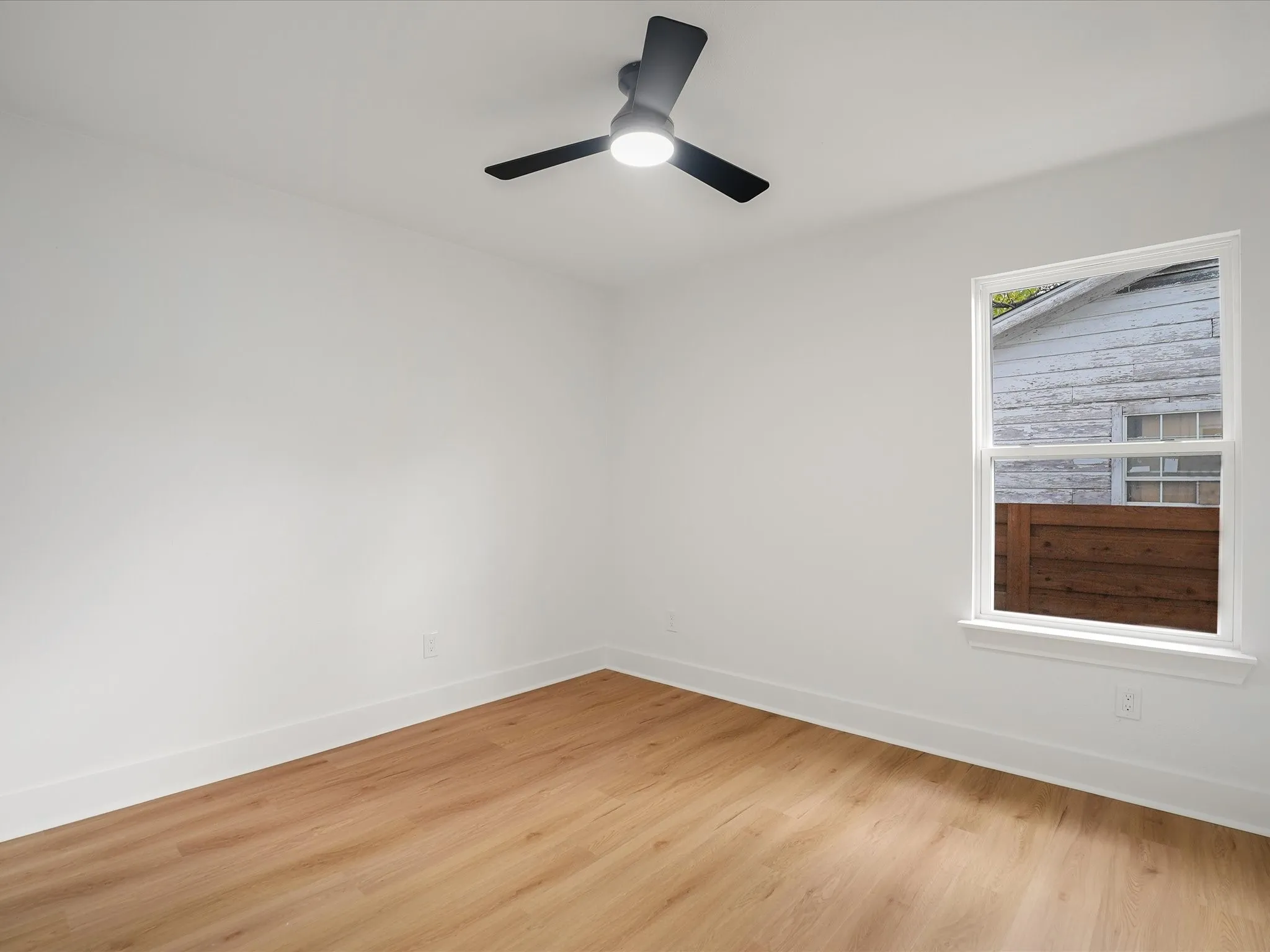 Neutral interior featuring wood-finish flooring, a matte black ceiling fan with integrated lighting, and a single-hung window
