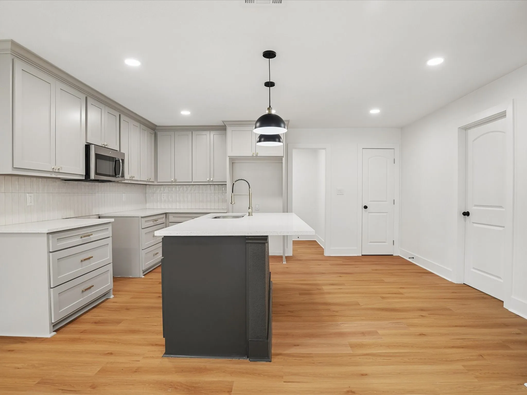 Kitchen featuring light grey shaker-style cabinetry, quartz countertops, a contrasting dark kitchen island, recessed lighting, and wood-finish flooring