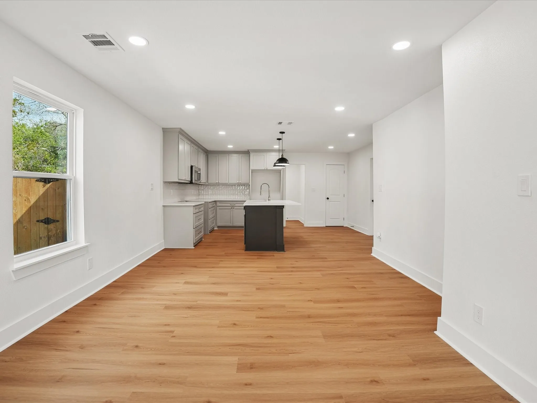 Open-concept kitchen featuring light-toned cabinetry, a dark-toned central island, recessed lighting, and wood-finish flooring