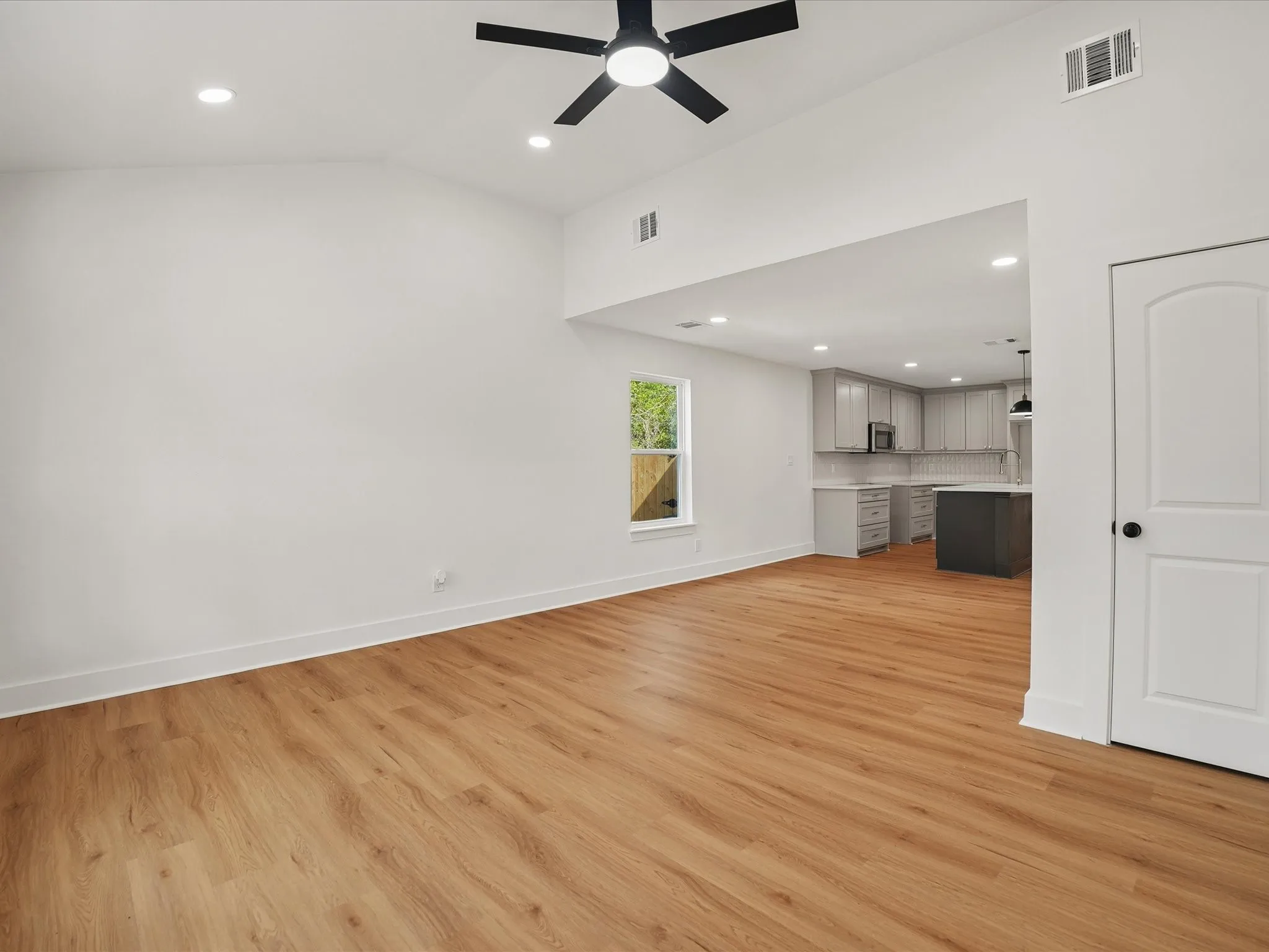 Vaulted ceiling featuring a central matte black ceiling fan, wood-finish flooring, recessed lighting, and a neutral color palette