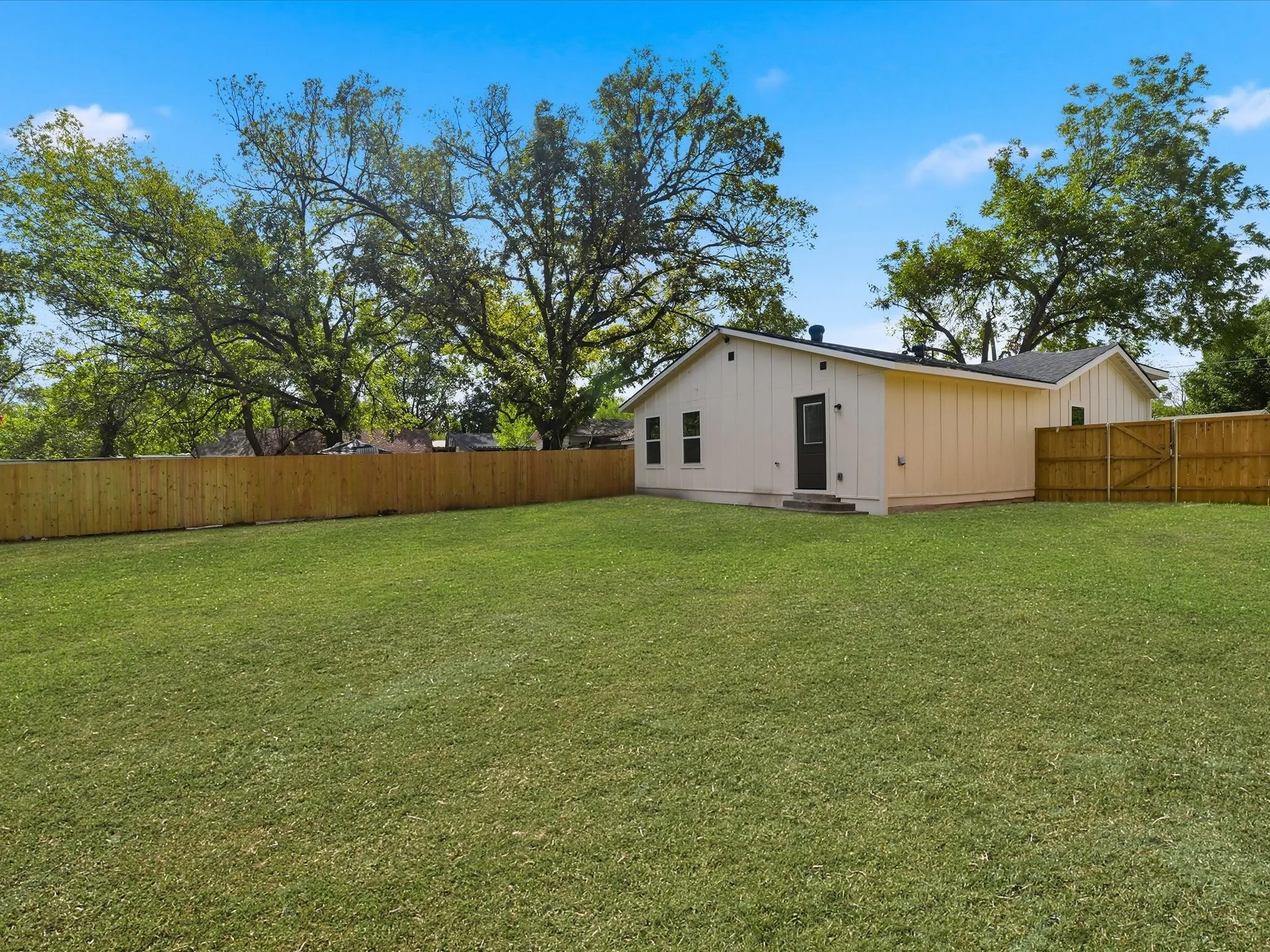 Expansive backyard featuring a manicured lawn, wood-panel fencing, and mature trees