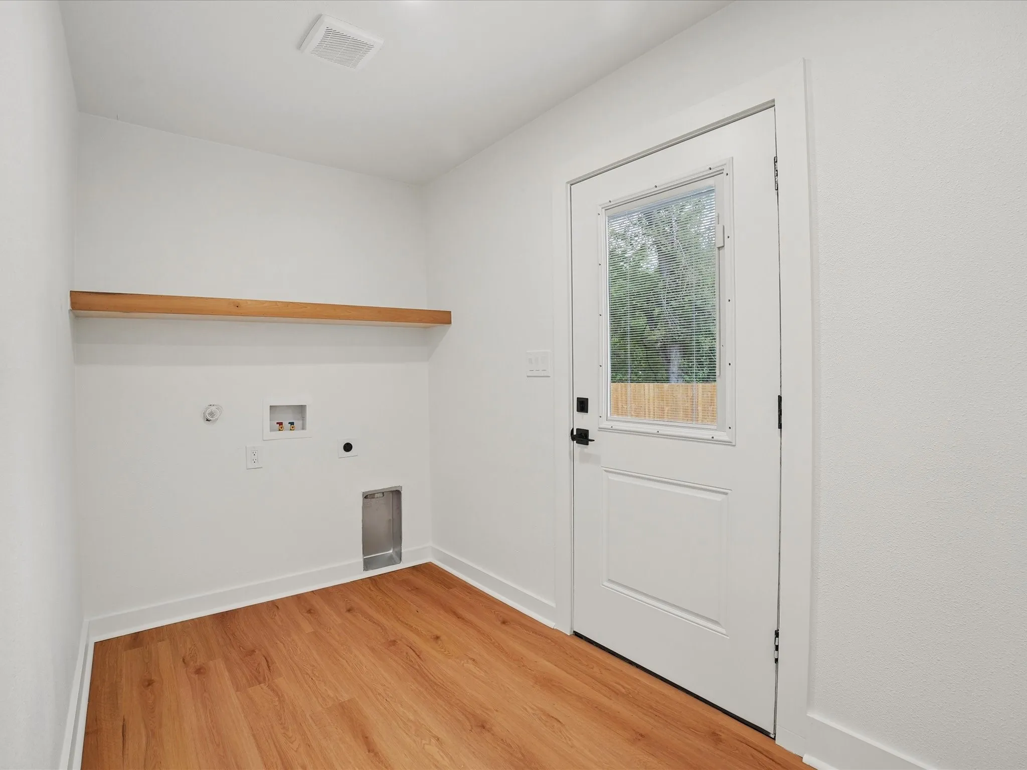 Utility space featuring wood-finish flooring, a wall-mounted floating wood shelf, and an exterior door with an integrated window