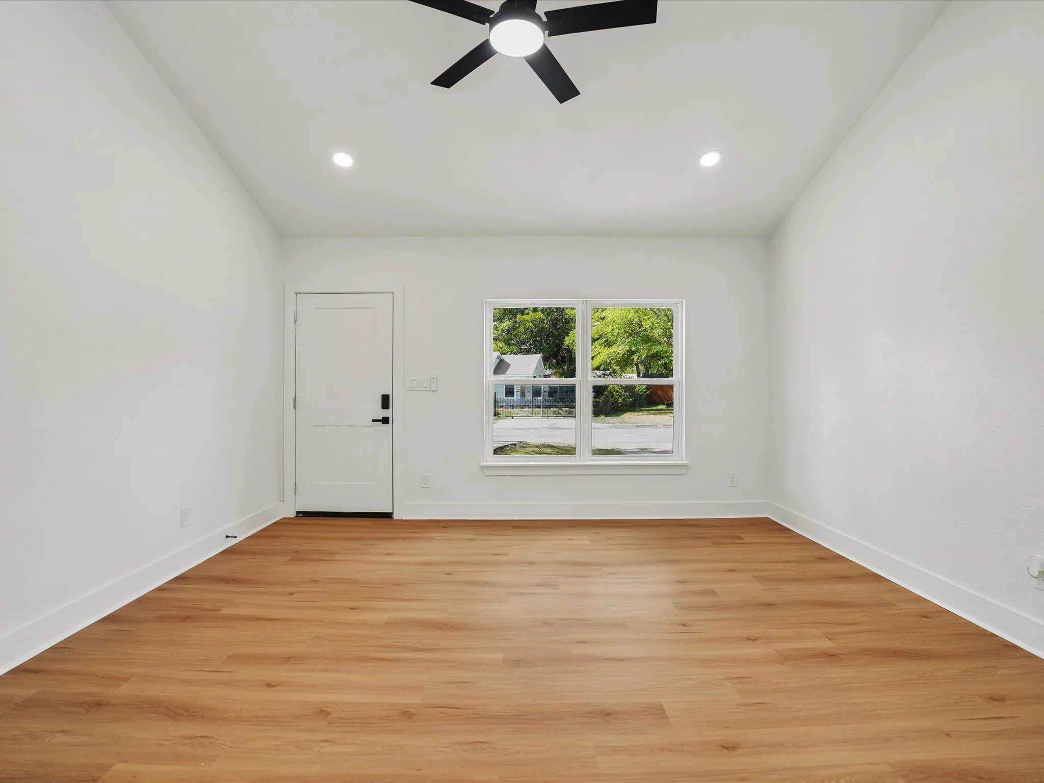 Vaulted ceiling featuring a central matte black ceiling fan, wood-finish flooring, recessed lighting, and a multi-pane window