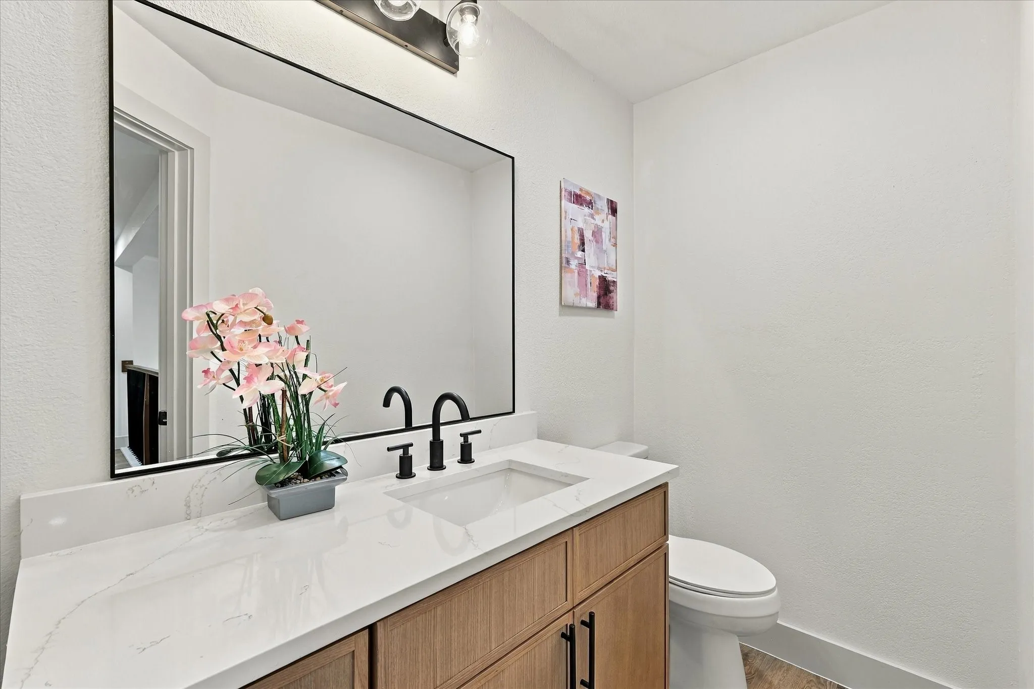 Vanity featuring a light wood-finish cabinet, white surface with veining, and a black-framed rectangular mirror, accented by a matte black faucet and multi-bulb industrial-style lighting