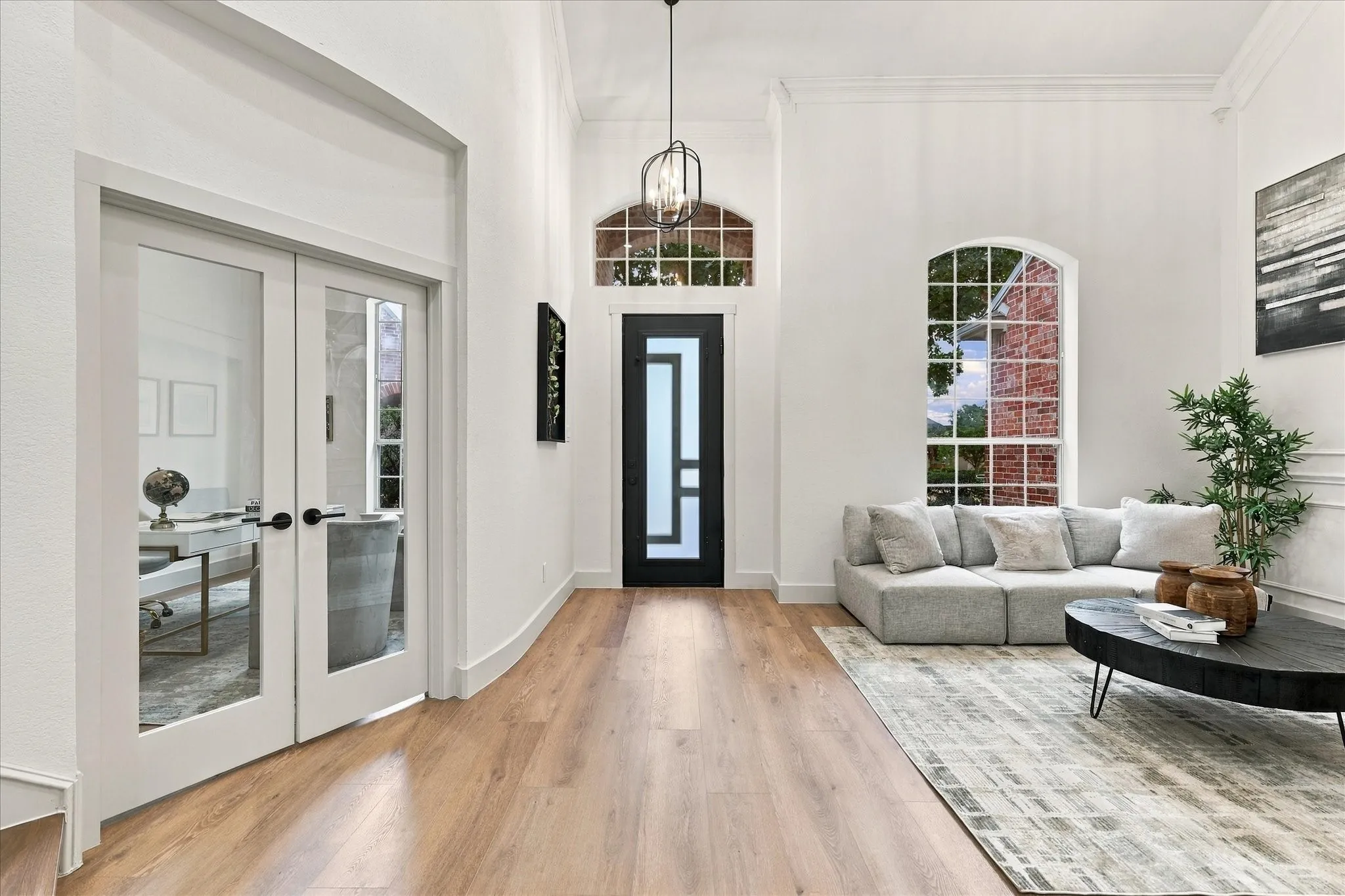 Foyer featuring high ceilings, wood-finish flooring, a contemporary front door with geometric glass panels, arched window, and dual glass-panel French doors