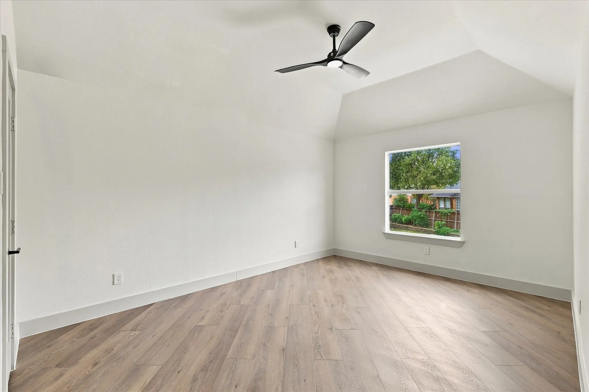 Vaulted ceiling featuring a matte black three-blade ceiling fan and wood-finish flooring