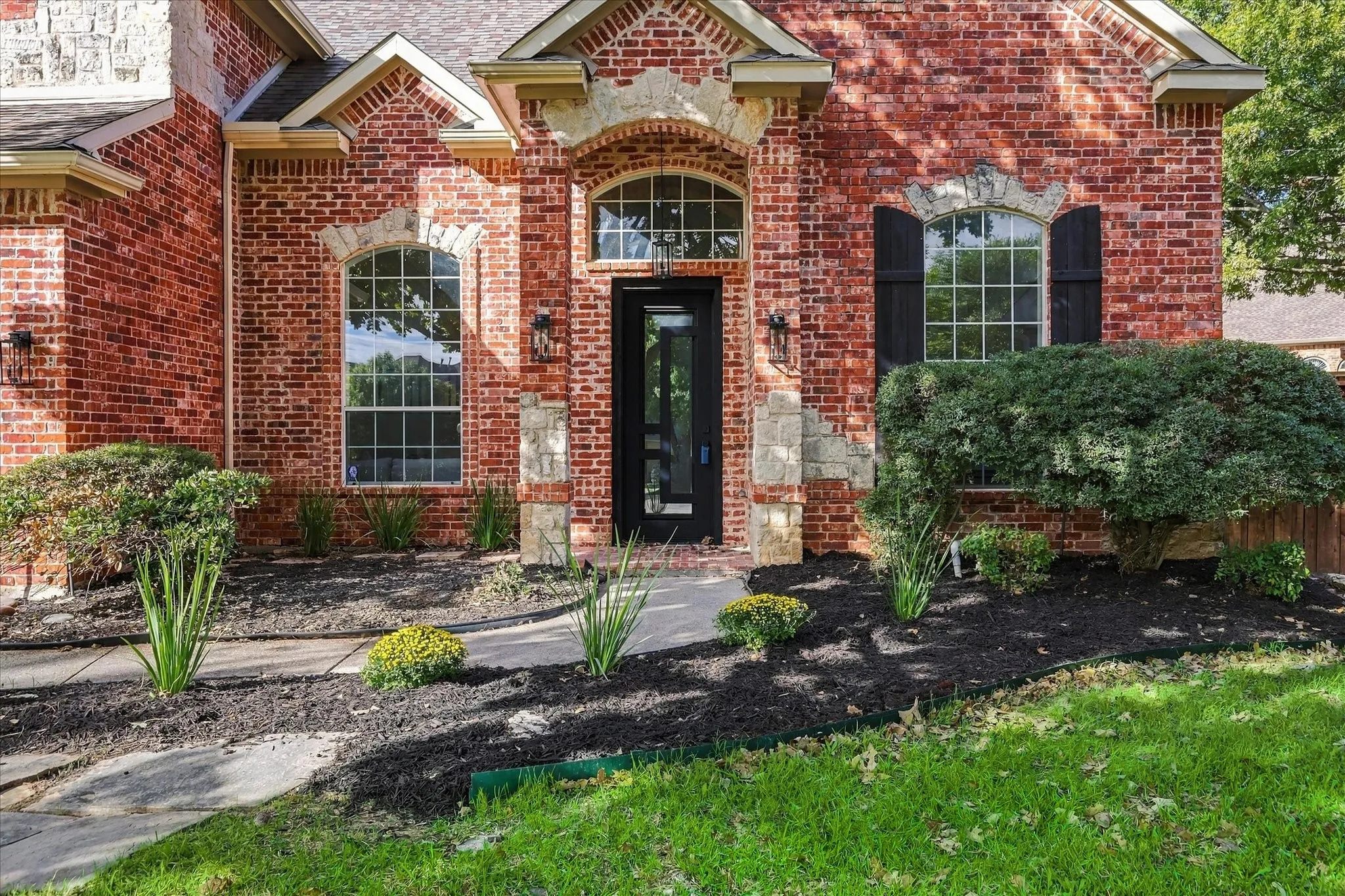Brick exterior featuring arched windows, stone masonry accents, black decorative shutters, and a covered entryway
