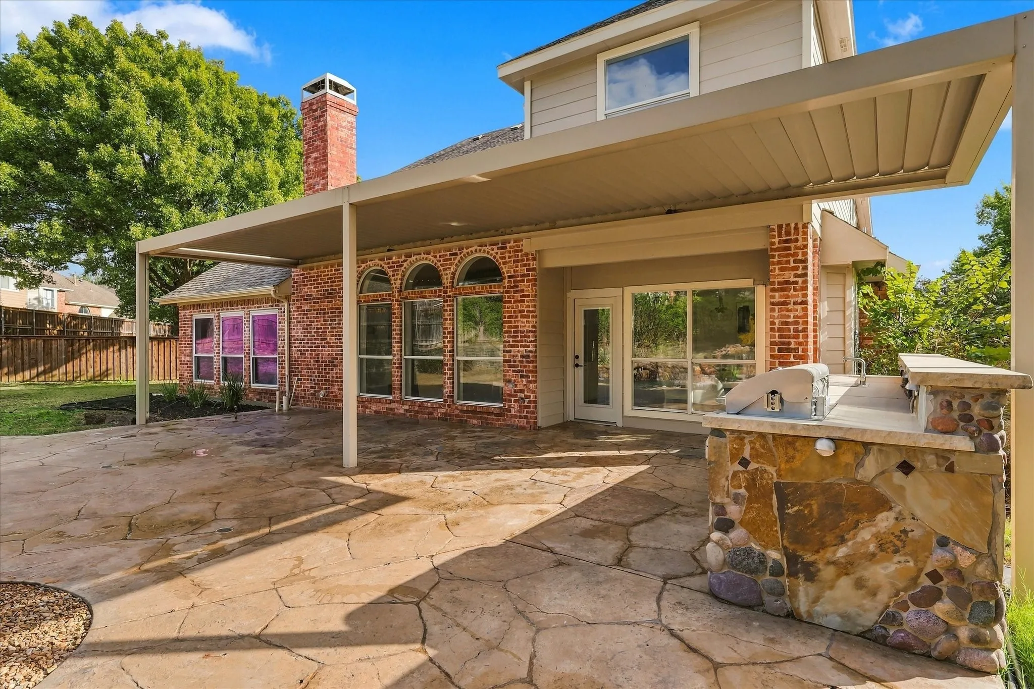 Rear patio featuring flagstone paving, a covered pergola, built-in stone grill station, brick chimney, and arched windows
