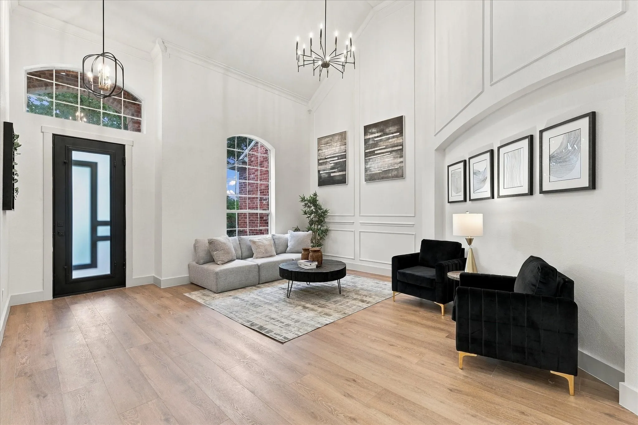 Entryway featuring vaulted ceilings, wood-finish flooring, wainscoting detail, arched windows, and a black-framed glass front door