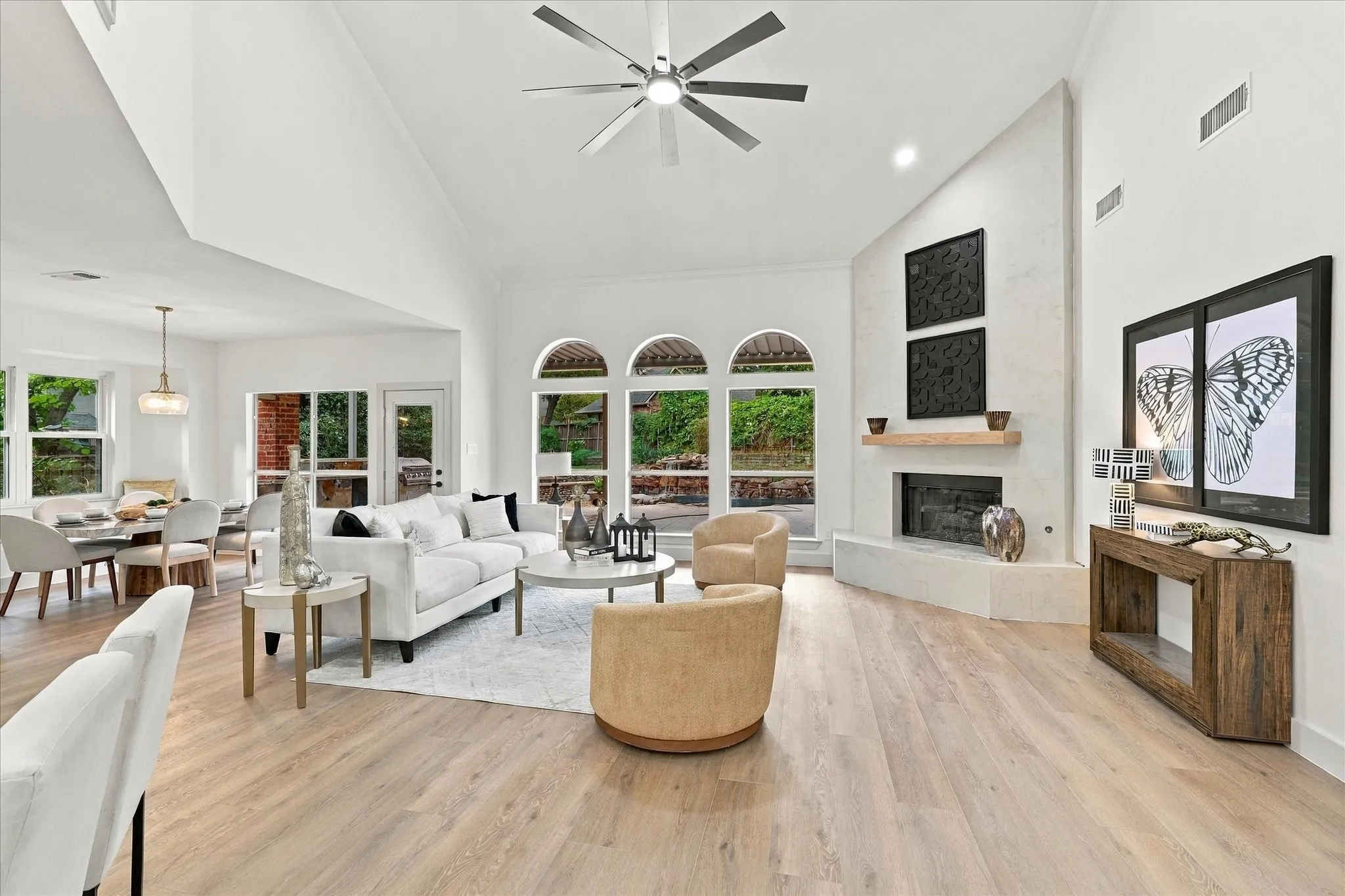 Vaulted ceilings with a multi-blade ceiling fan, expansive wood-finish flooring, floor-to-ceiling stone-faced fireplace with a natural wood mantel, and arched windows