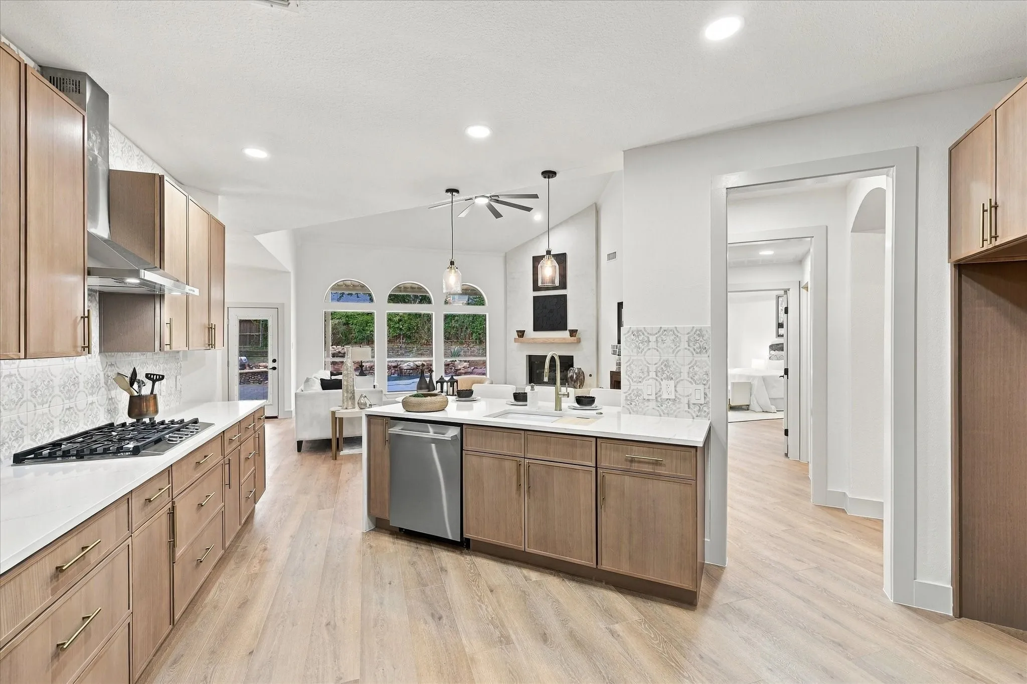 Kitchen featuring light wood-finish cabinetry, white countertops, a stainless steel dishwasher, gas cooktop, and patterned tile backsplash